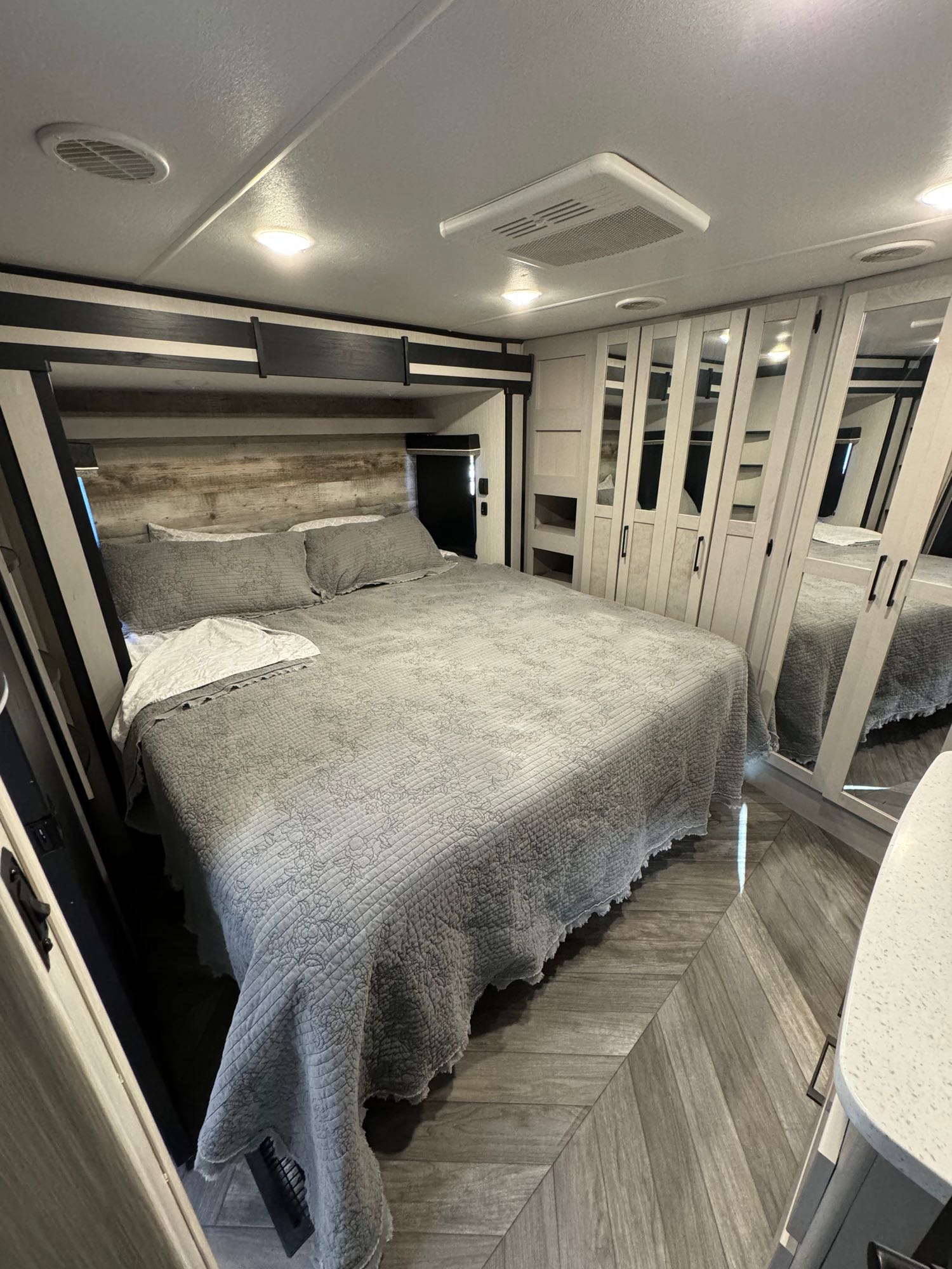 Modern RV rental bedroom with a comfortable bed, built-in mirrored wardrobe, and overhead AC. Contemporary and practical space.. Heartland Cyclone 2022
