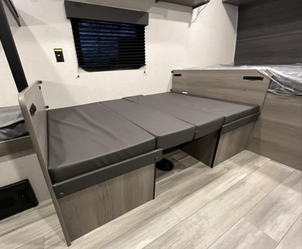 RV rental interior showing a versatile dinette that converts into a bed, featuring sleek gray cushions and wood-look finishes.. Keystone RV Hideout 2024