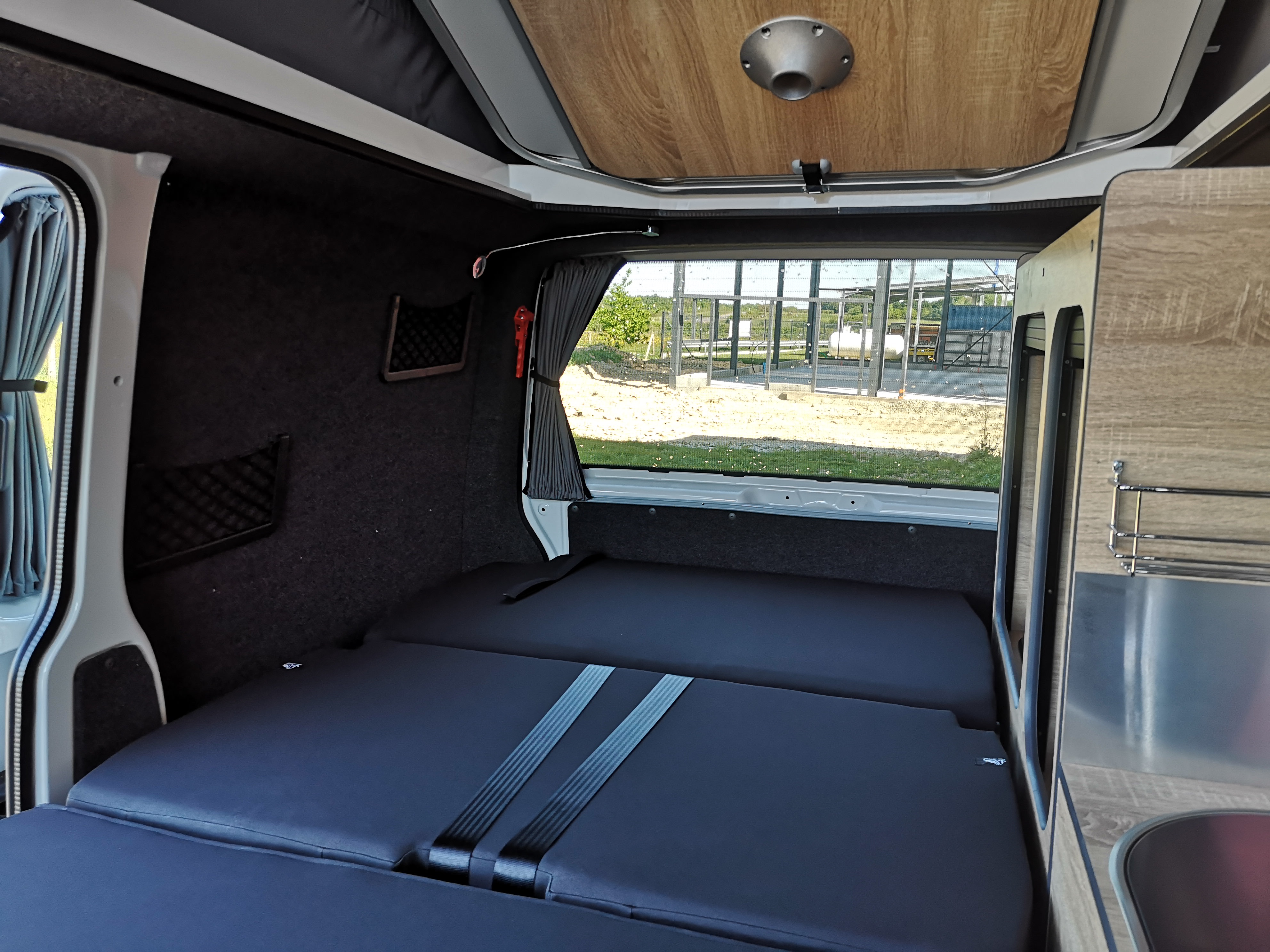 This compact RV rental camper interior features a plush bed, wood-paneled pop-top, window with curtains, and a practical kitchen.. Volkswagen Globe Trotteur 2024