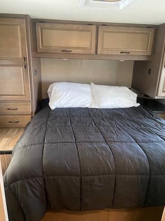 This RV rental bedroom offers a comfortable bed with a gray comforter, white pillows, and built-in storage cabinets.. Thor Majestic 2019