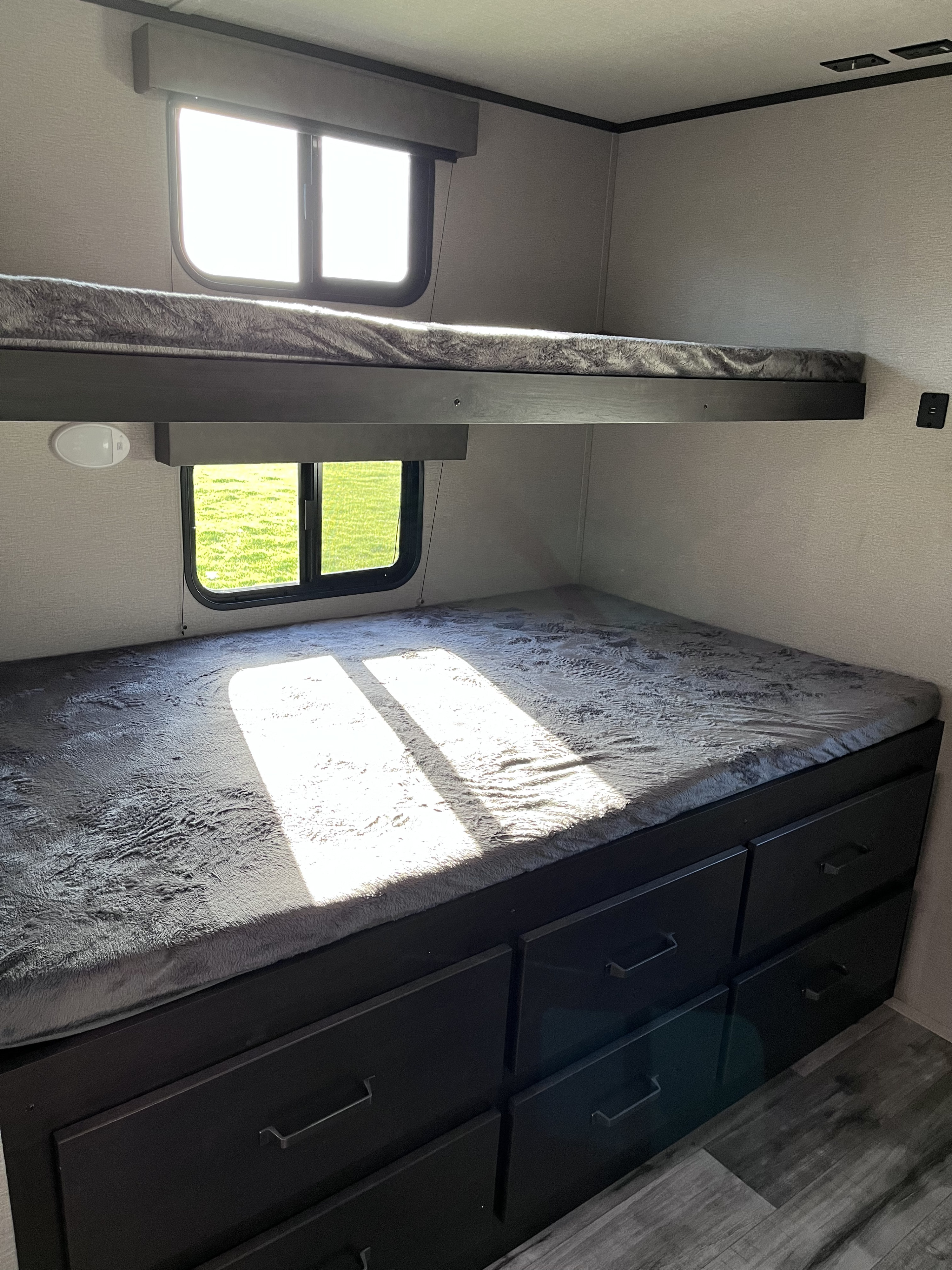 Modern RV rental bunk beds with built-in storage drawers, illuminated by sunlight.. Grand Design Transcend Xplor 2023