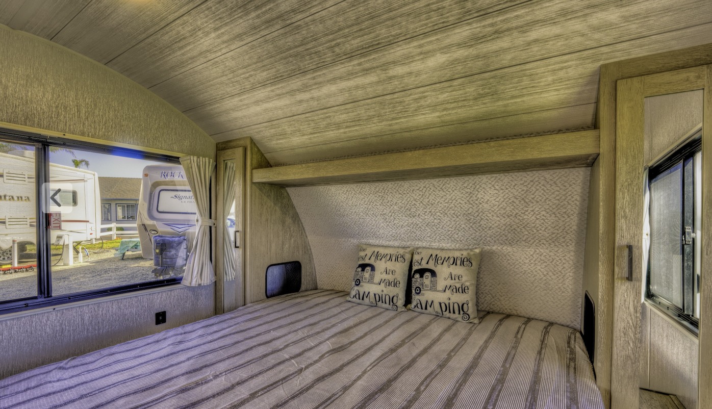 This RV rental bedroom features a comfy bed with striped bedding and "camping" pillows, plus a large window view.. SALEM CRUISE LITE PLATINUM 28VBLX 2024