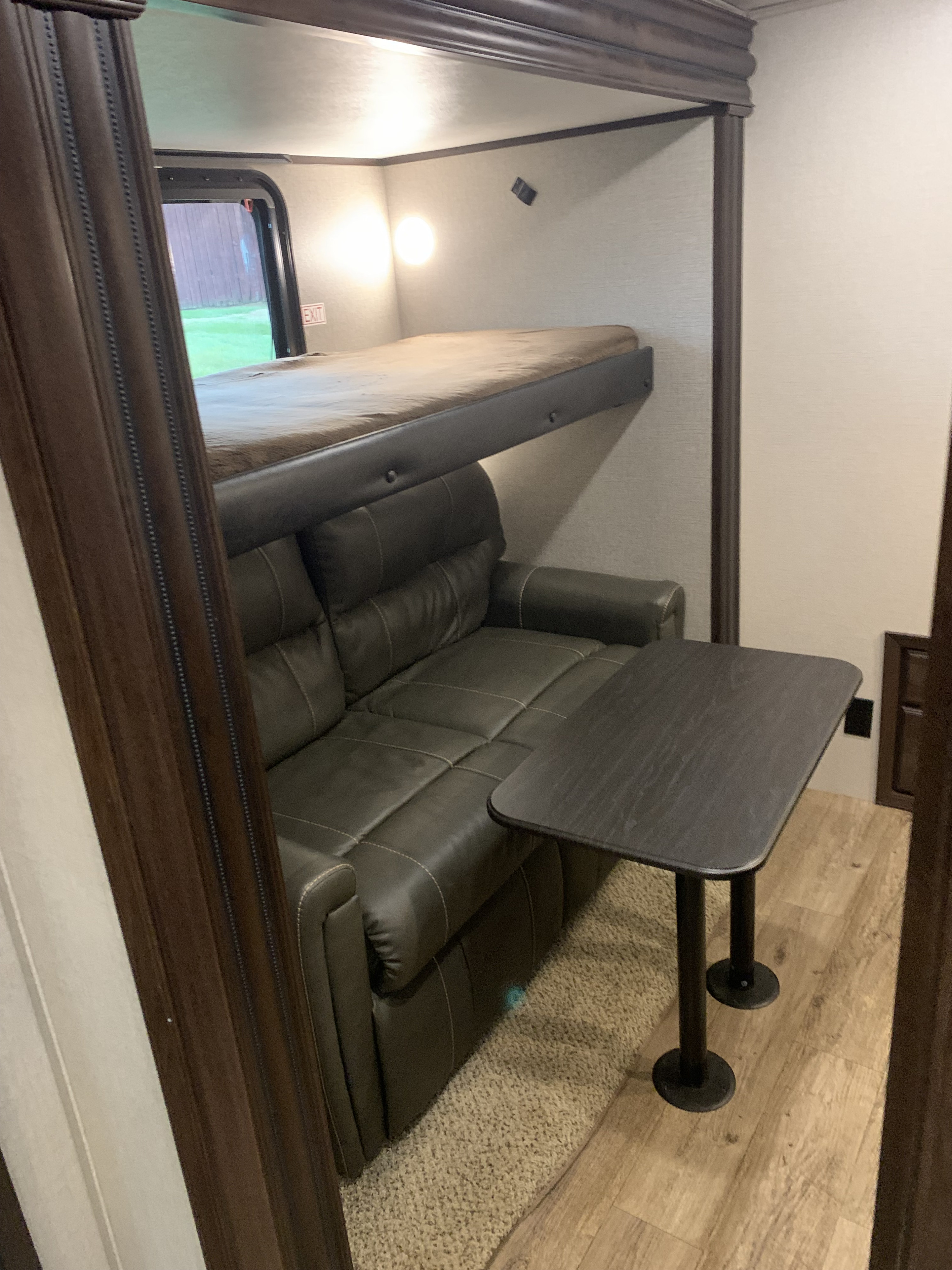 Inside an RV rental: a compact living area with a brown leather sofa, bunk bed above, and a small table.. Jayco North Point 2020