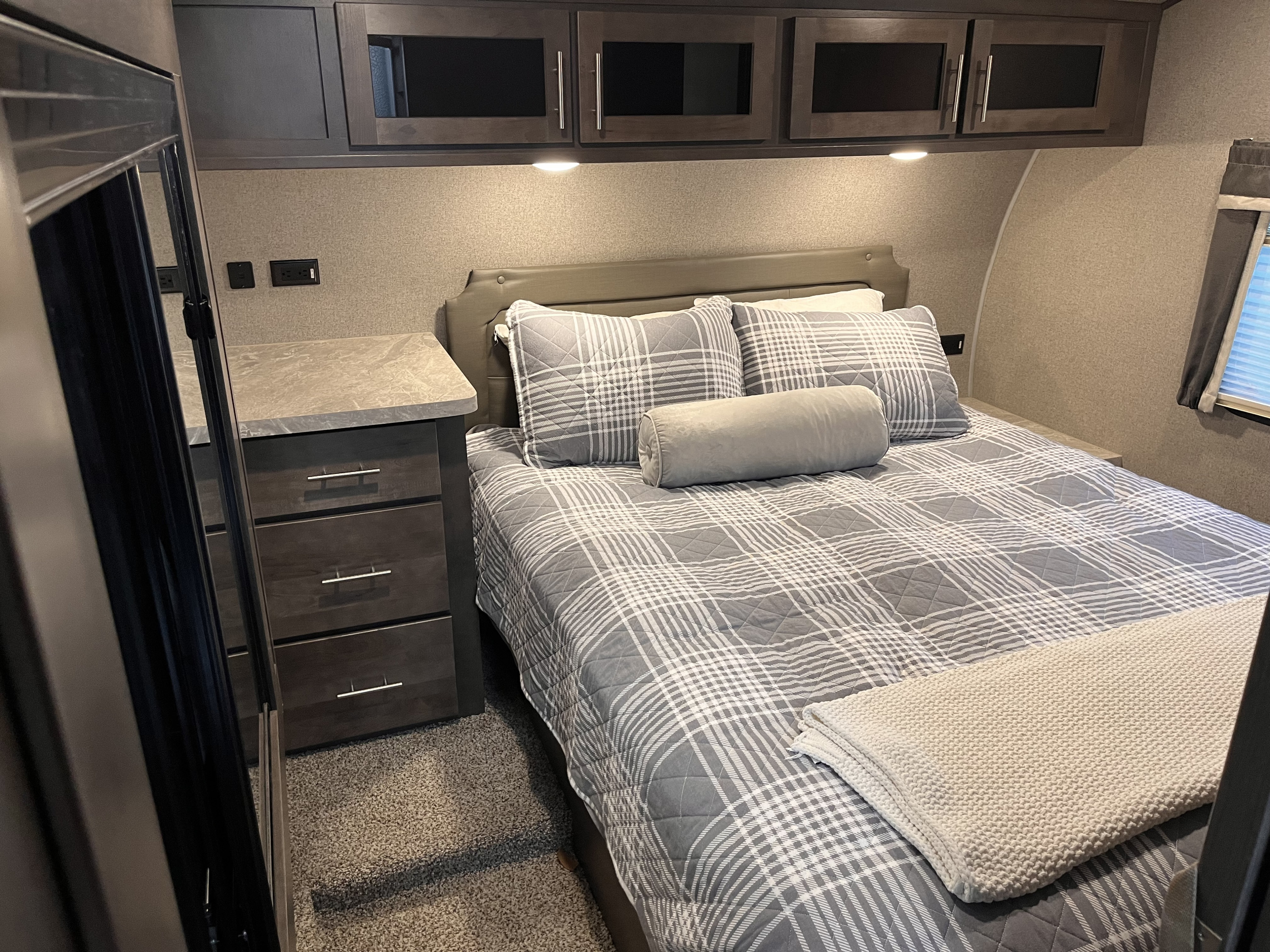 Relax in this cozy RV rental bedroom. Features a comfy bed with plaid bedding, ample storage, and bedside power outlets.. Forest River Rockwood Ultra Lite 2020
