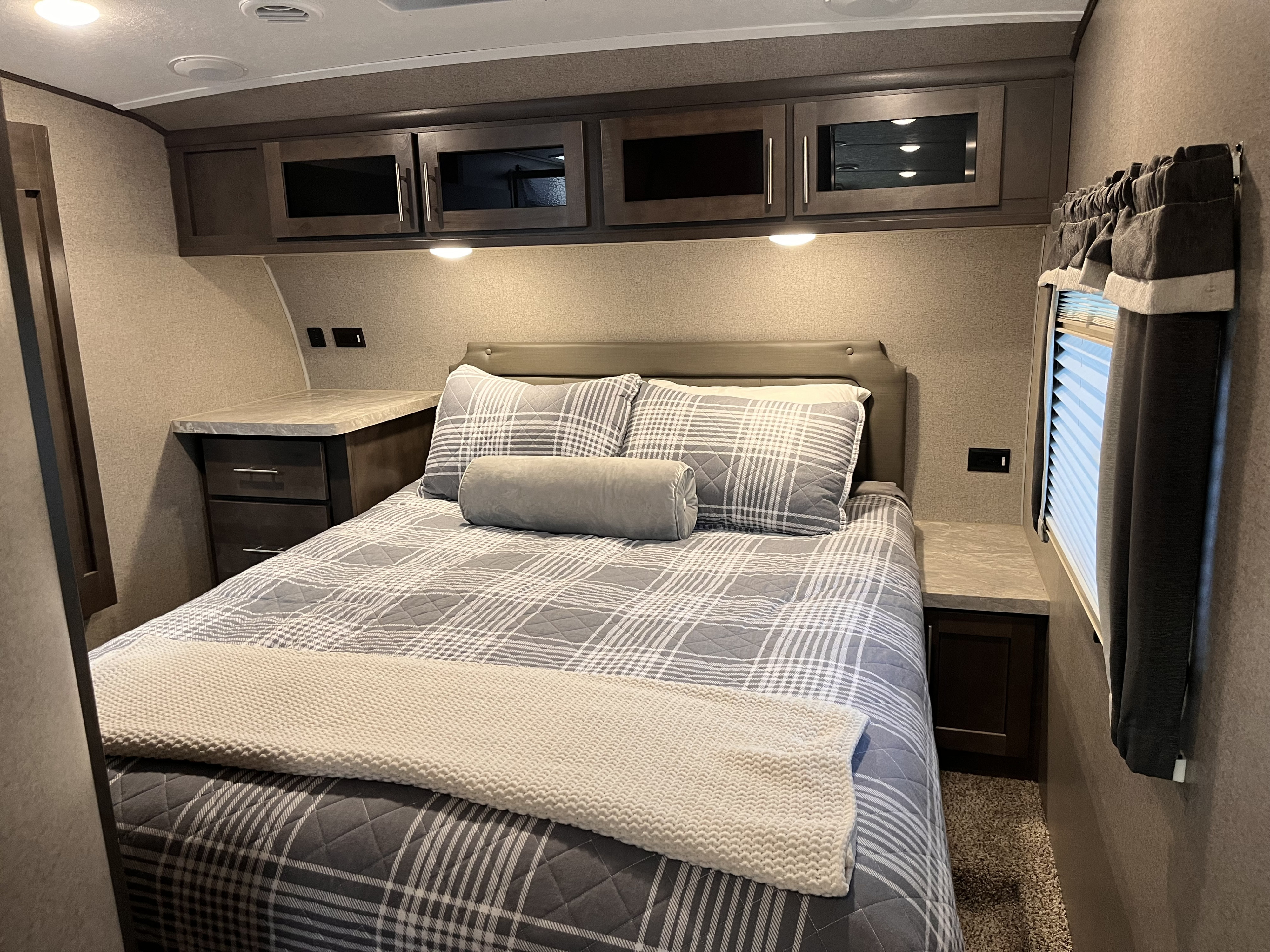 This inviting RV rental bedroom features a made bed with plaid comforter, overhead cabinets, and bedside tables.. Forest River Rockwood Ultra Lite 2020