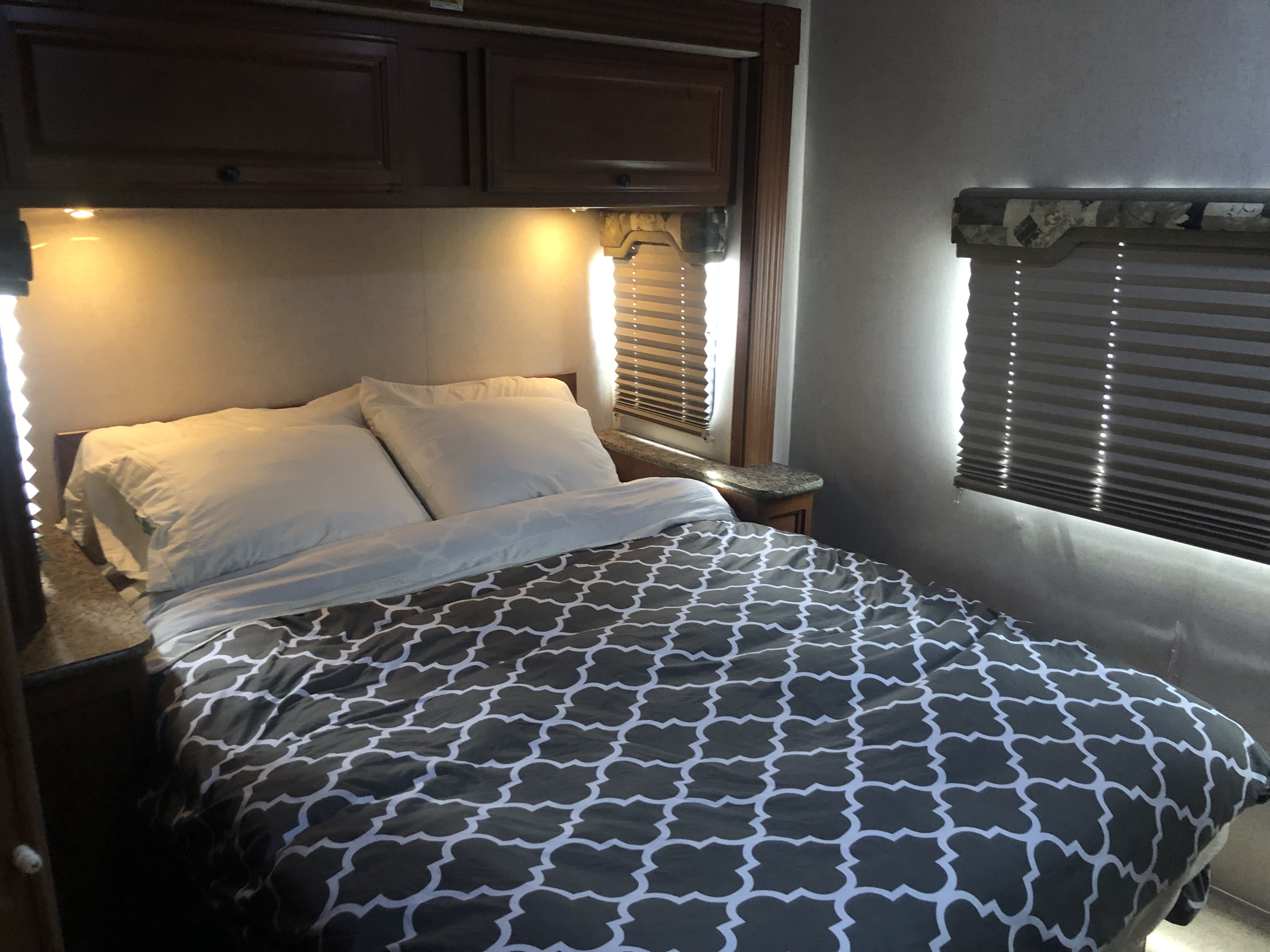 Cozy RV rental bedroom with patterned comforter, white pillows, overhead cabinets, and blinds, highlighting compact comfort.. Jamboree Sport 2010