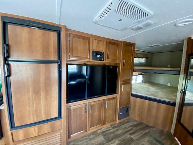 RV rental interior with large fridge, TV, overhead AC, and comfortable bunk beds, all in a warm wood-toned finish.. Avenger ATI 2018