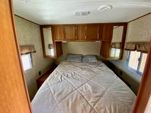 Cozy RV rental bedroom with bed, overhead cabinets, and mirrored side walls. Ideal for comfortable travel.. Avenger ATI 2018