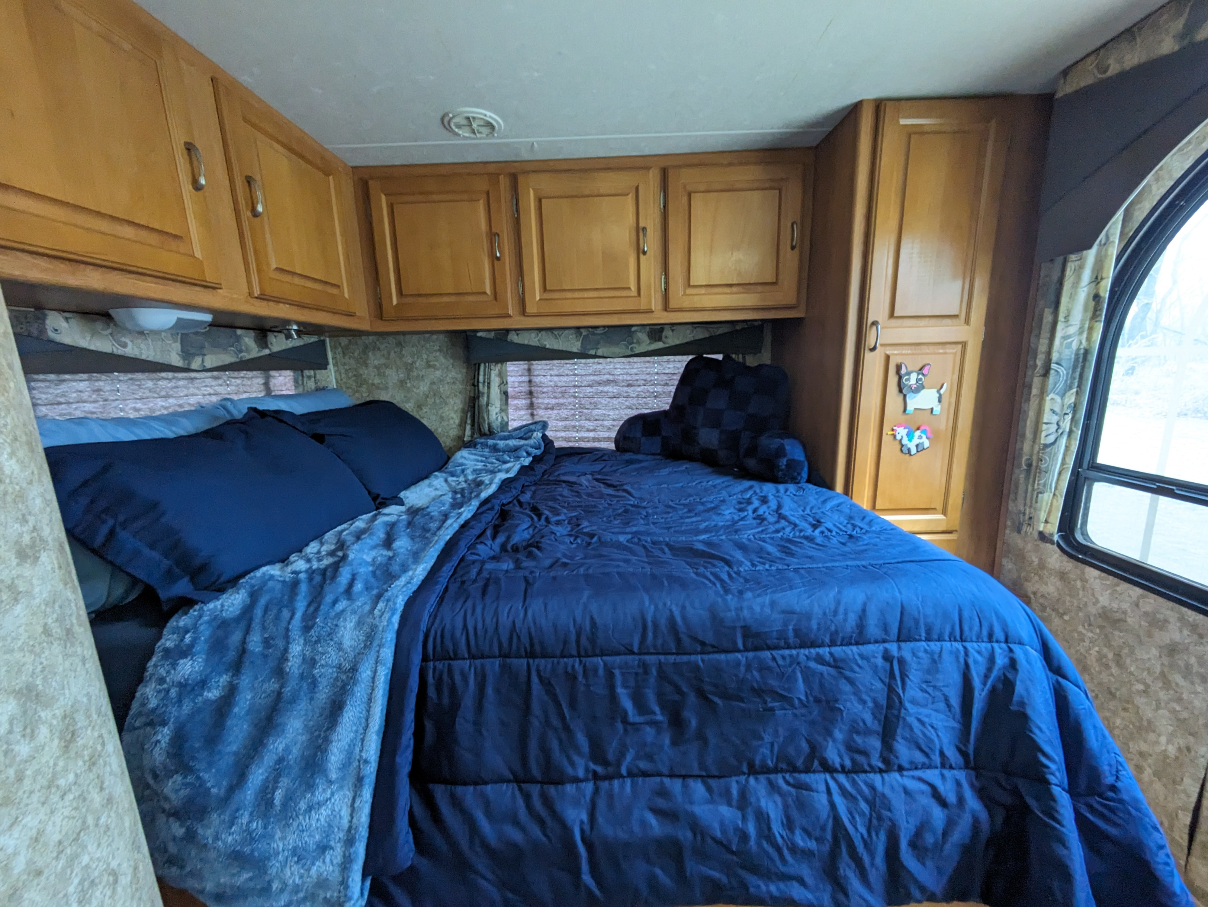 Cozy RV rental bedroom with blue bedding, overhead wood cabinets, and an arched window view.. Coachmen Freelander Deluxe/Premier 2005