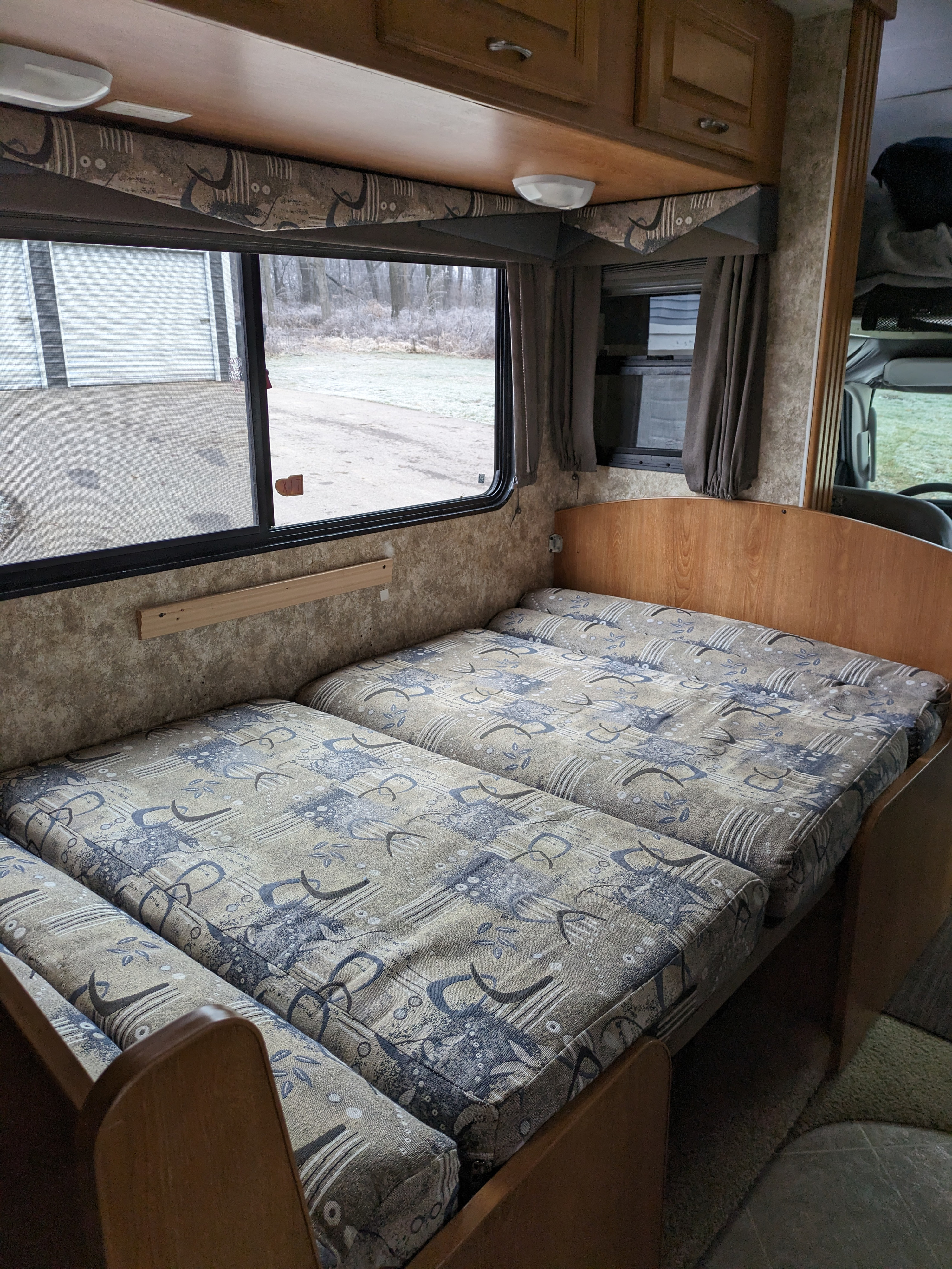 Inside an RV rental: a compact, modular sleeping area with patterned cushions. Window offers a glimpse of a wintery outdoor scene.. Coachmen Freelander Deluxe/Premier 2005