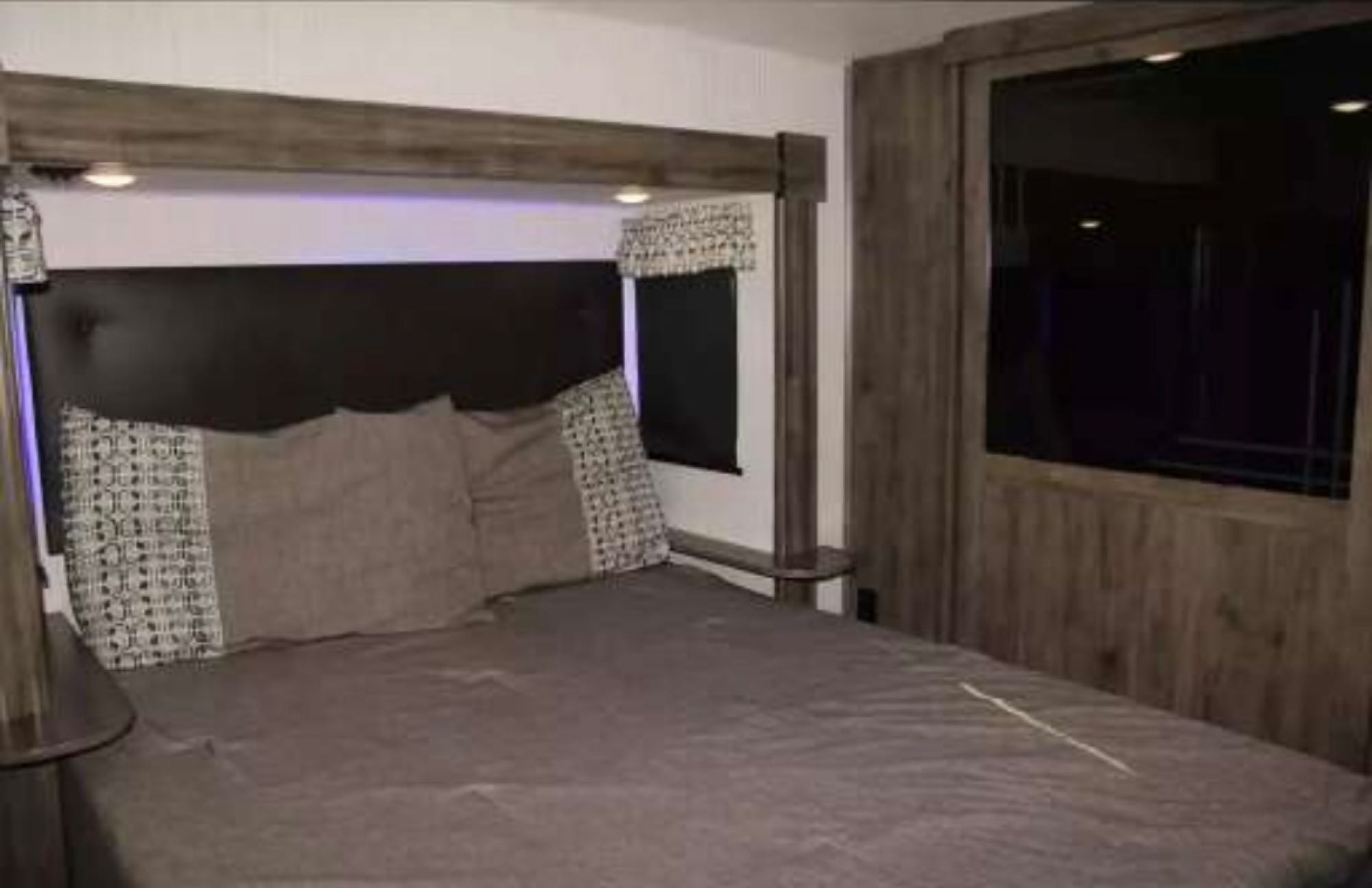 Cozy RV rental bedroom features a large bed with pillows, overhead lighting, and a mounted TV, perfect for mobile comfort.. Forest River Sierra 2021