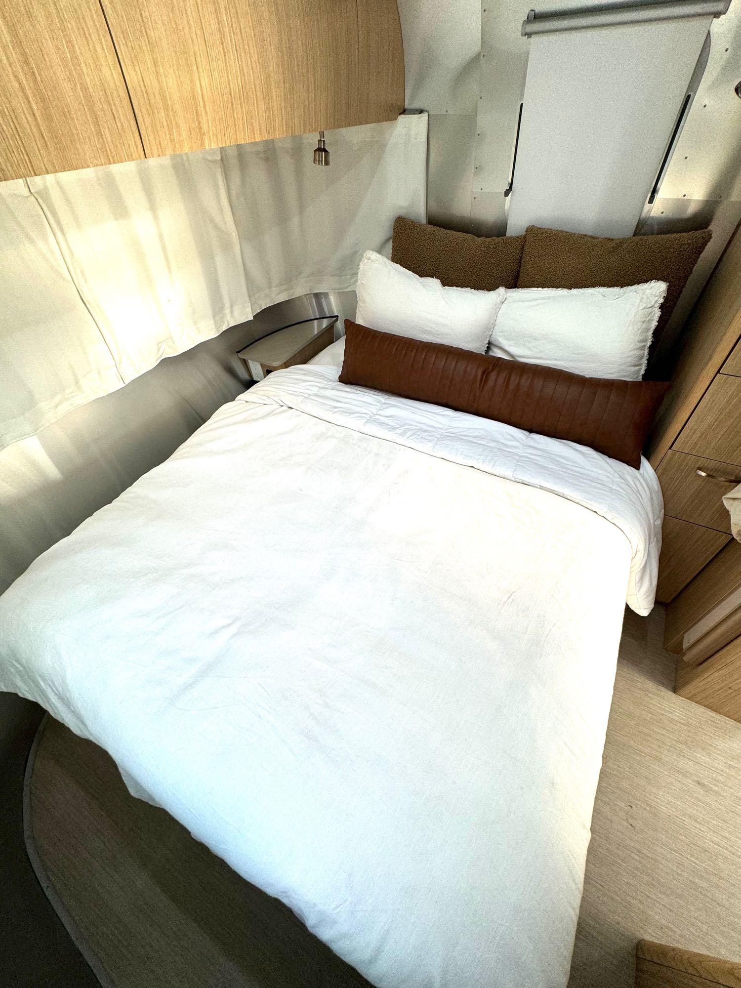 Cozy RV rental bedroom with white bedding, brown pillows, and wooden accents. Ideal for travel comfort.. Airstream Flying Cloud 2017