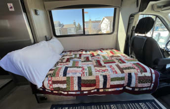 Cozy RV rental interior with a comfortable bed, patchwork quilt, and large window for scenic travel views.. Forest River Coachmen Cross Trail XL 2022