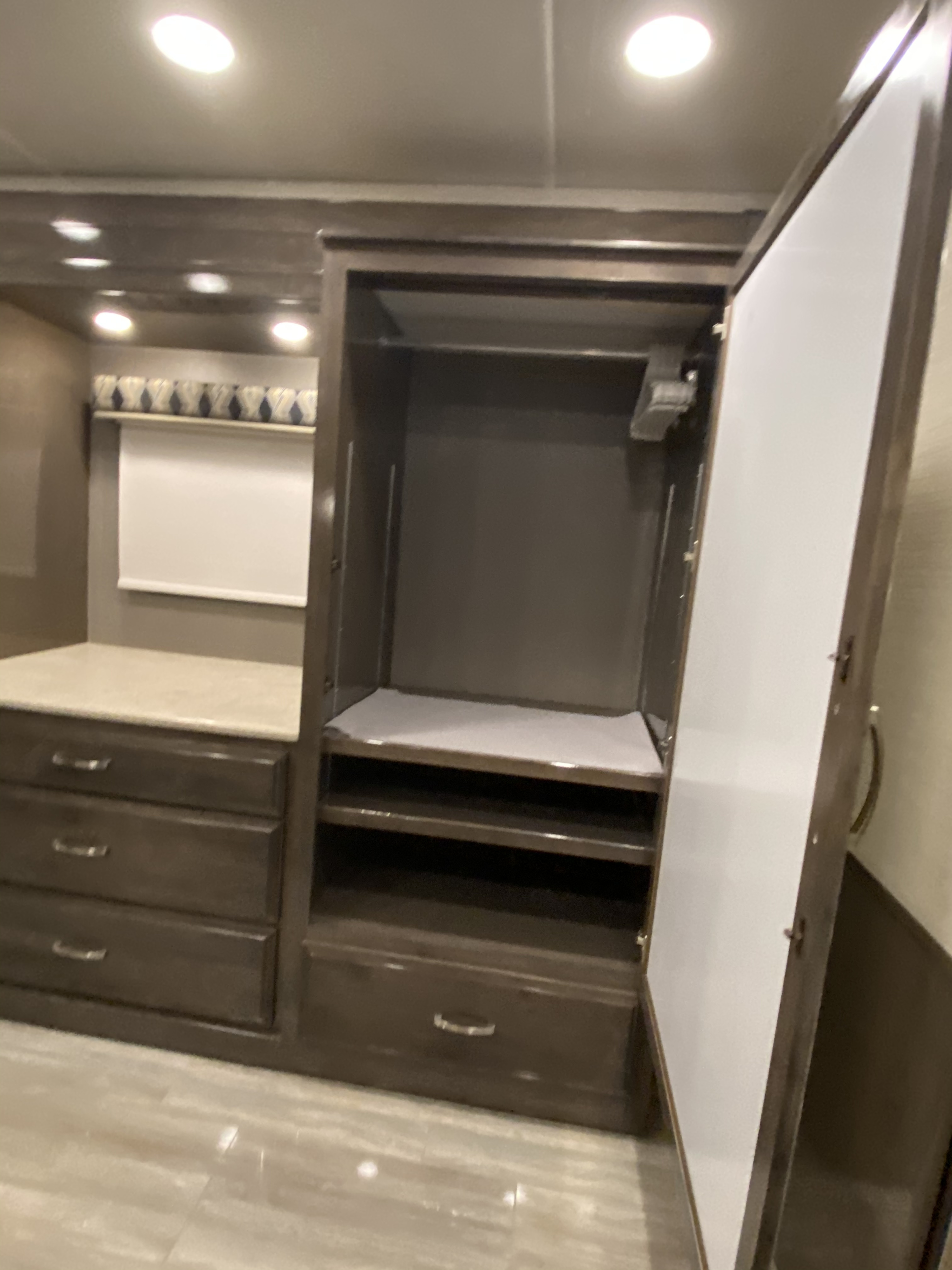 RV rental bedroom interior features a dark wood wardrobe with a hanging rod and shelves, plus a dresser with multiple drawers.. Entegra Coach Reatta XL 2020