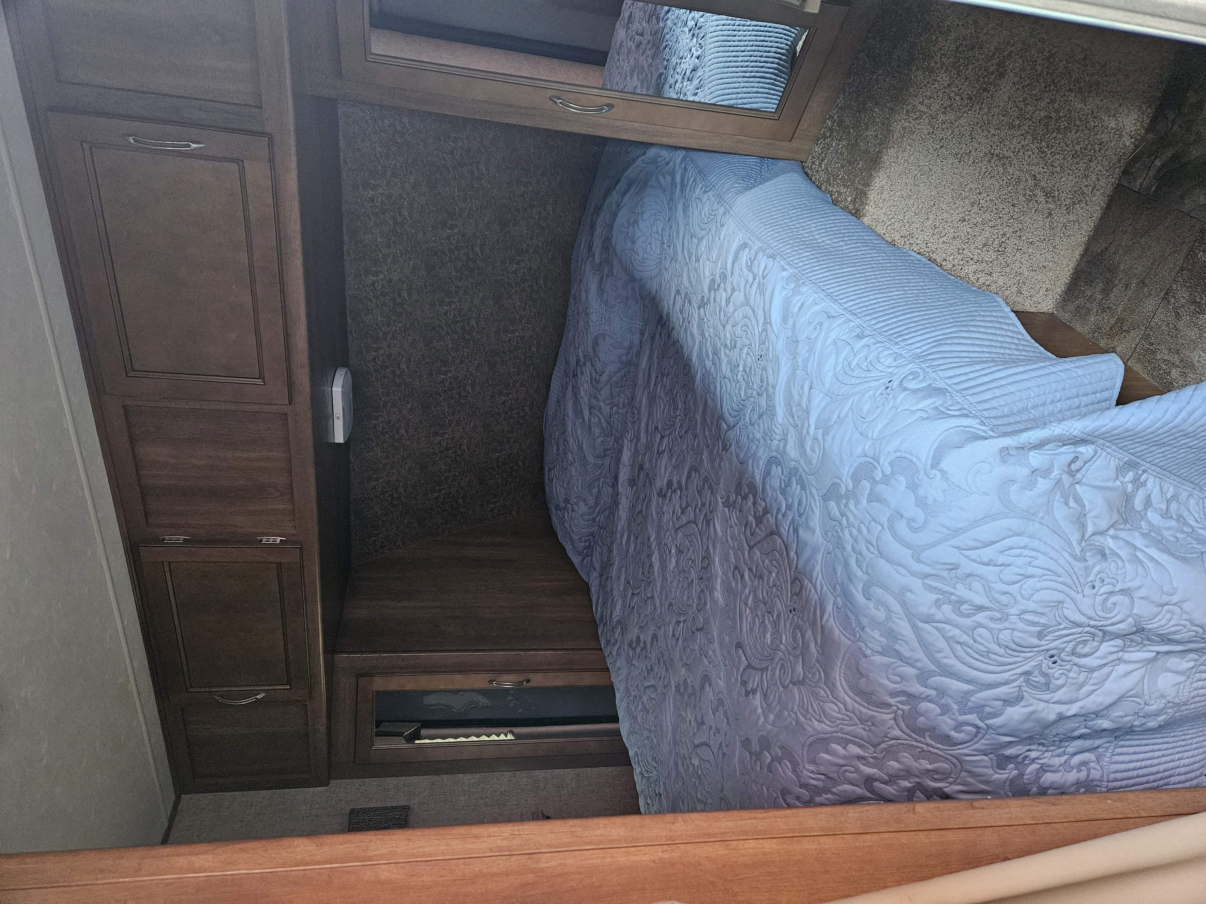 Cozy RV rental bedroom featuring a bed with a patterned comforter, built-in wooden storage, and a mirror.. Coachmen Apex 50th Anniversary 2015