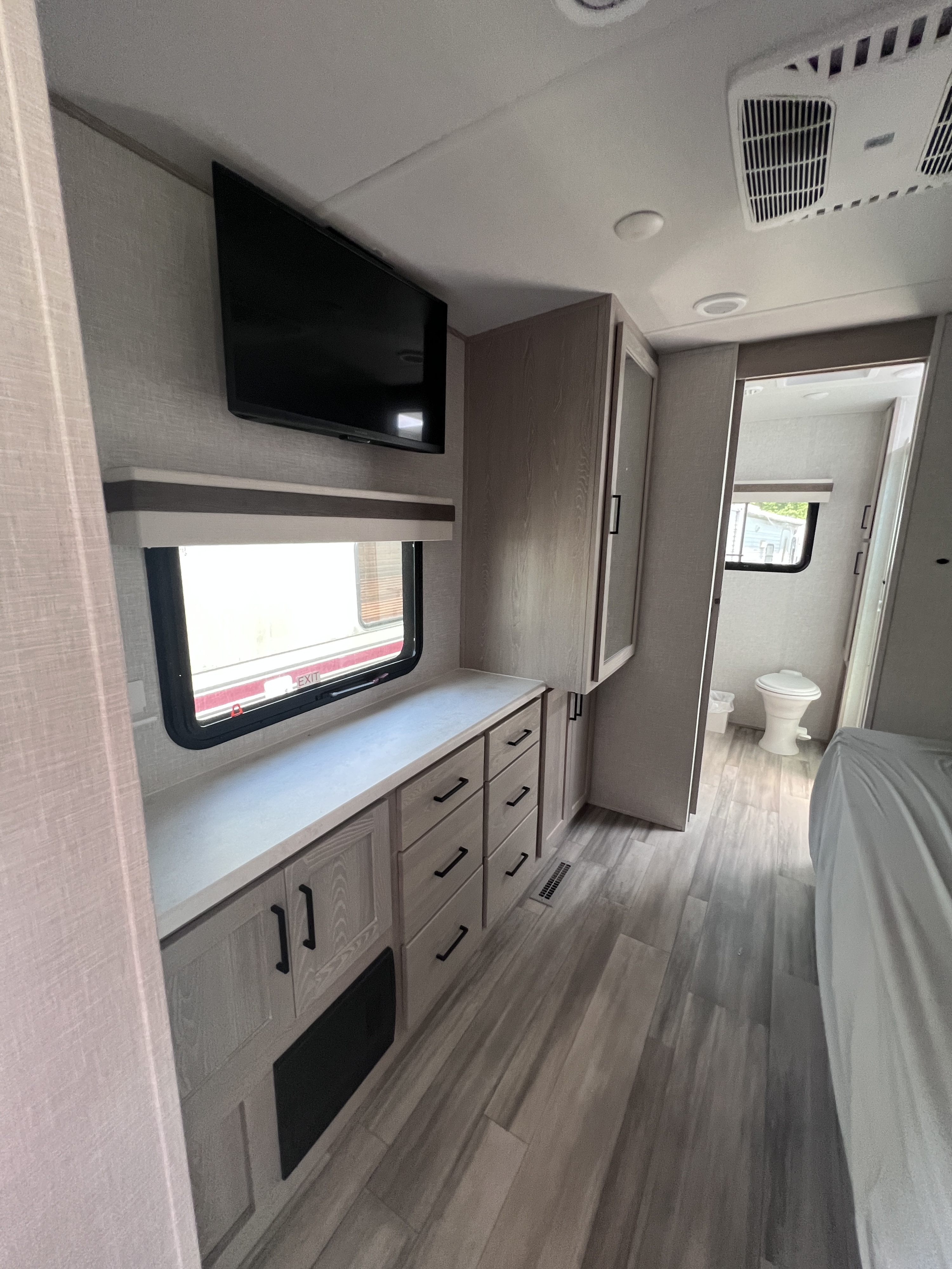 Cozy RV rental bedroom featuring a TV, built-in storage, and a peek into the bright bathroom.. Forest River Rockwood Signature 2022