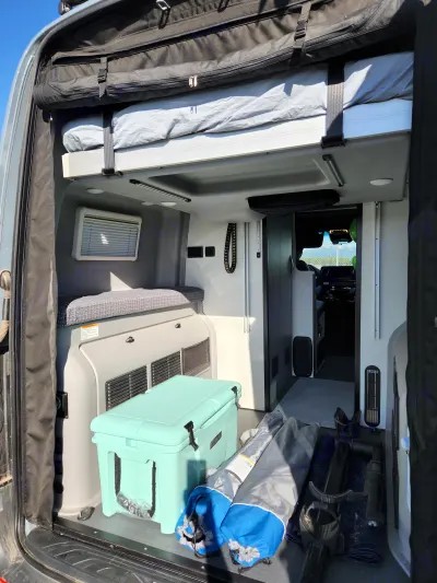 Explore this RV rental van's organized interior: an overhead bed, cooler, and gear ready for your next trip.. Winnebago Revel 2022