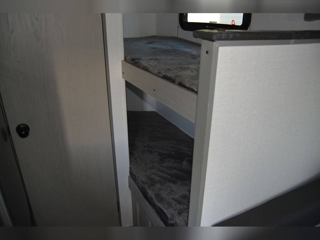 RV rental interior: A bright, compact sleeping area with two bunk beds and dark mattresses, beside a light wood-grain door.. Coachmen Clipper 2024