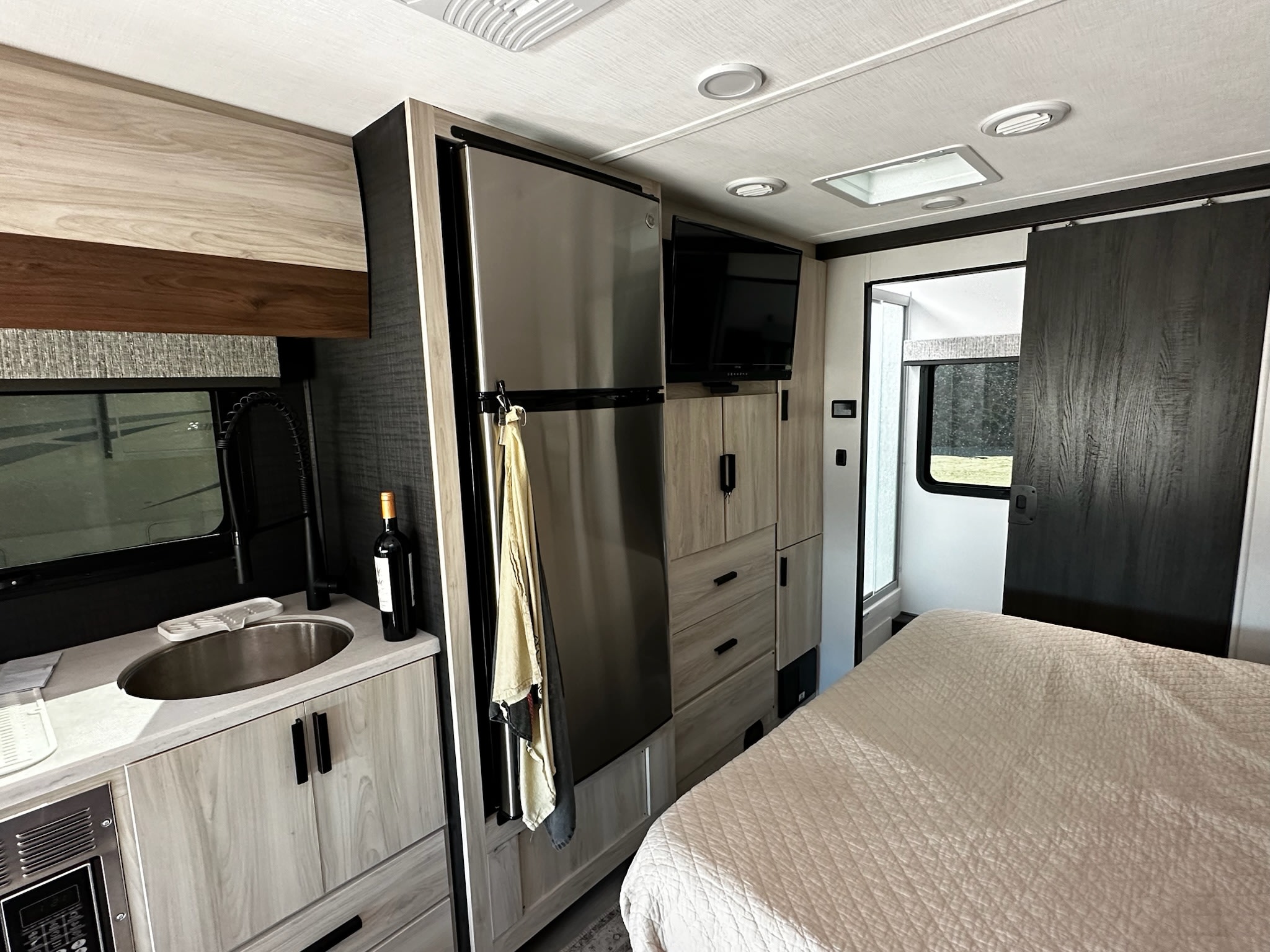 Cozy RV rental interior showing a compact kitchen with a sink, stainless steel fridge, TV, and comfortable bed area.. Forest River Mercedes 3500XD 2401T 2023