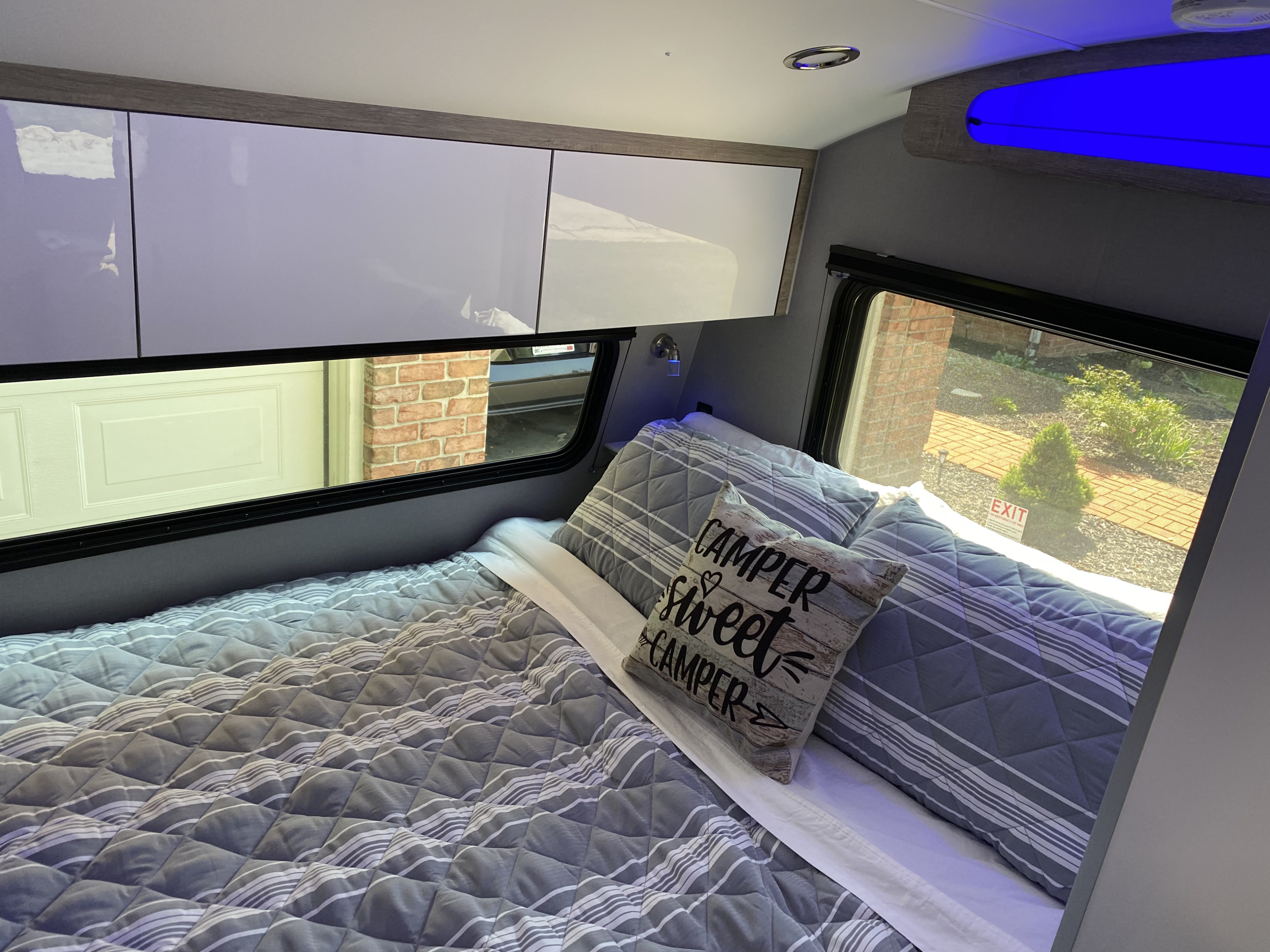 Cozy RV rental bedroom with striped bedding, "CAMPER sweet CAMPER" pillow, overhead cabinets, and outdoor views.. InTech Sol Horizon 2023
