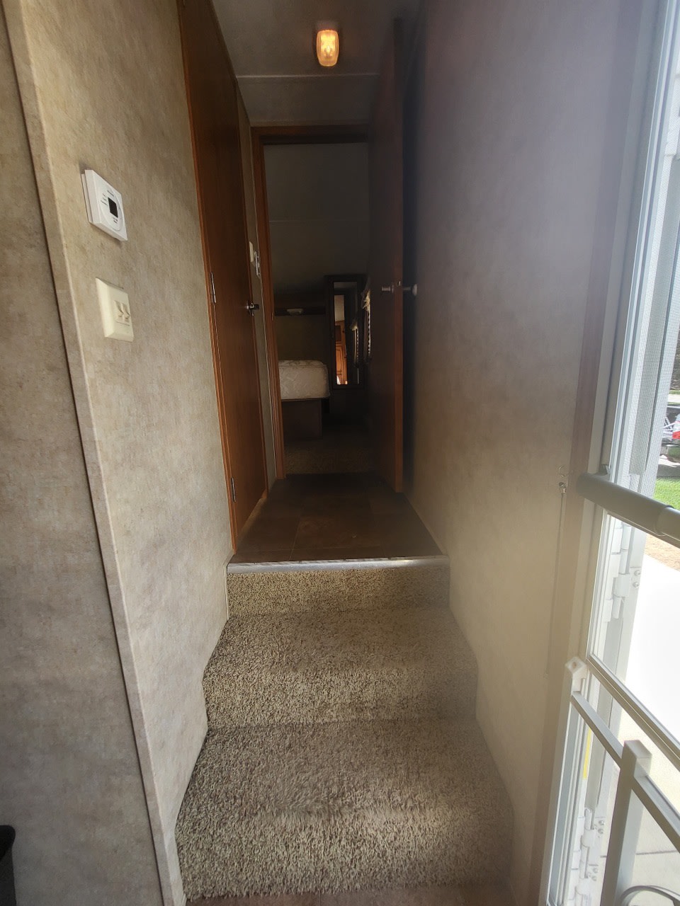 RV rental interior: Carpeted steps ascend into a narrow RV hallway leading to a bedroom. Thermostat visible on the left wall.. Forest River Palomino Sabre Silhouette 2013