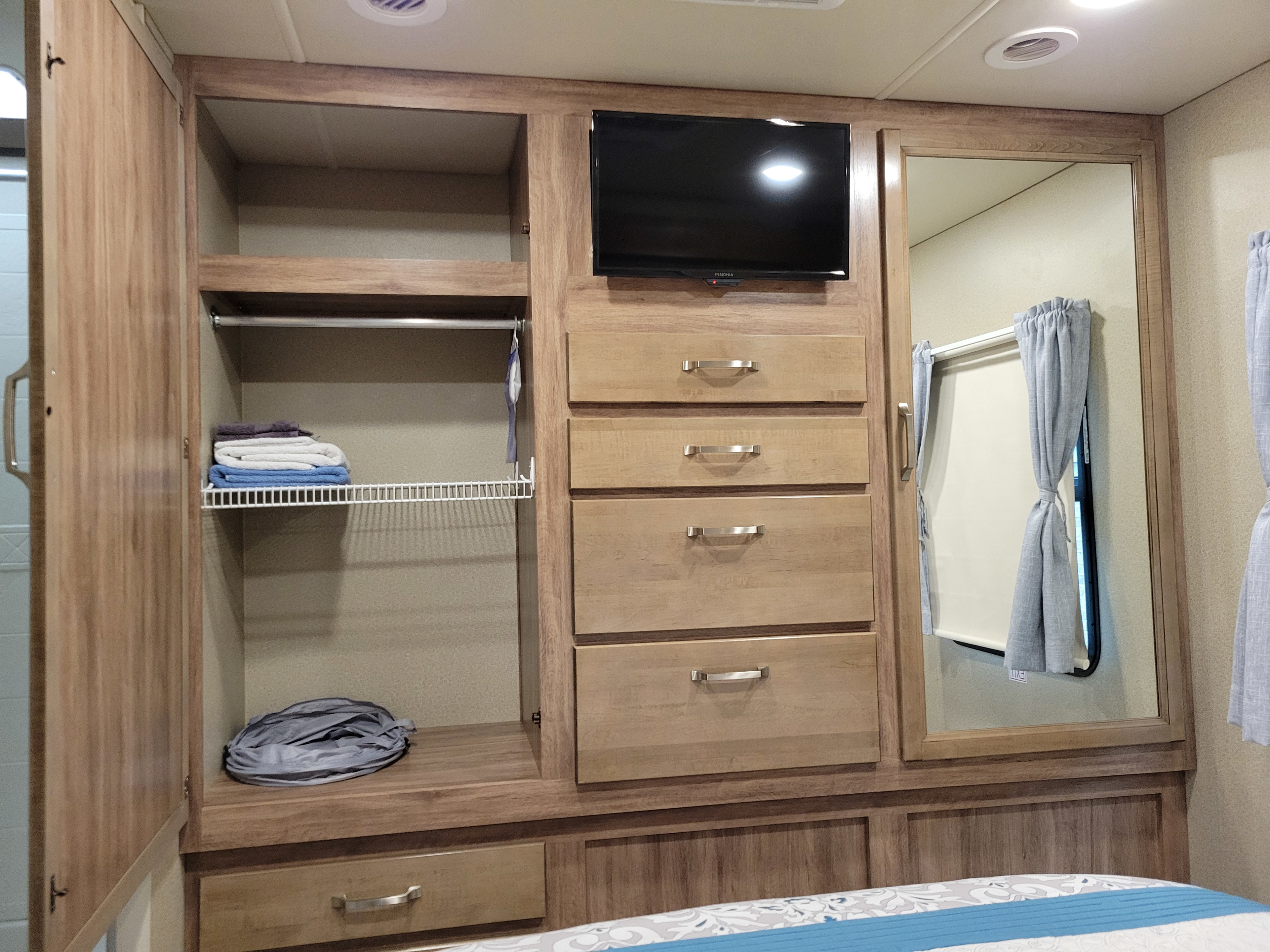 Inside an RV rental: a compact bedroom with wardrobe, mounted TV, multiple storage drawers, and full-length mirror.. Jayco Greyhawk Prestige 2019