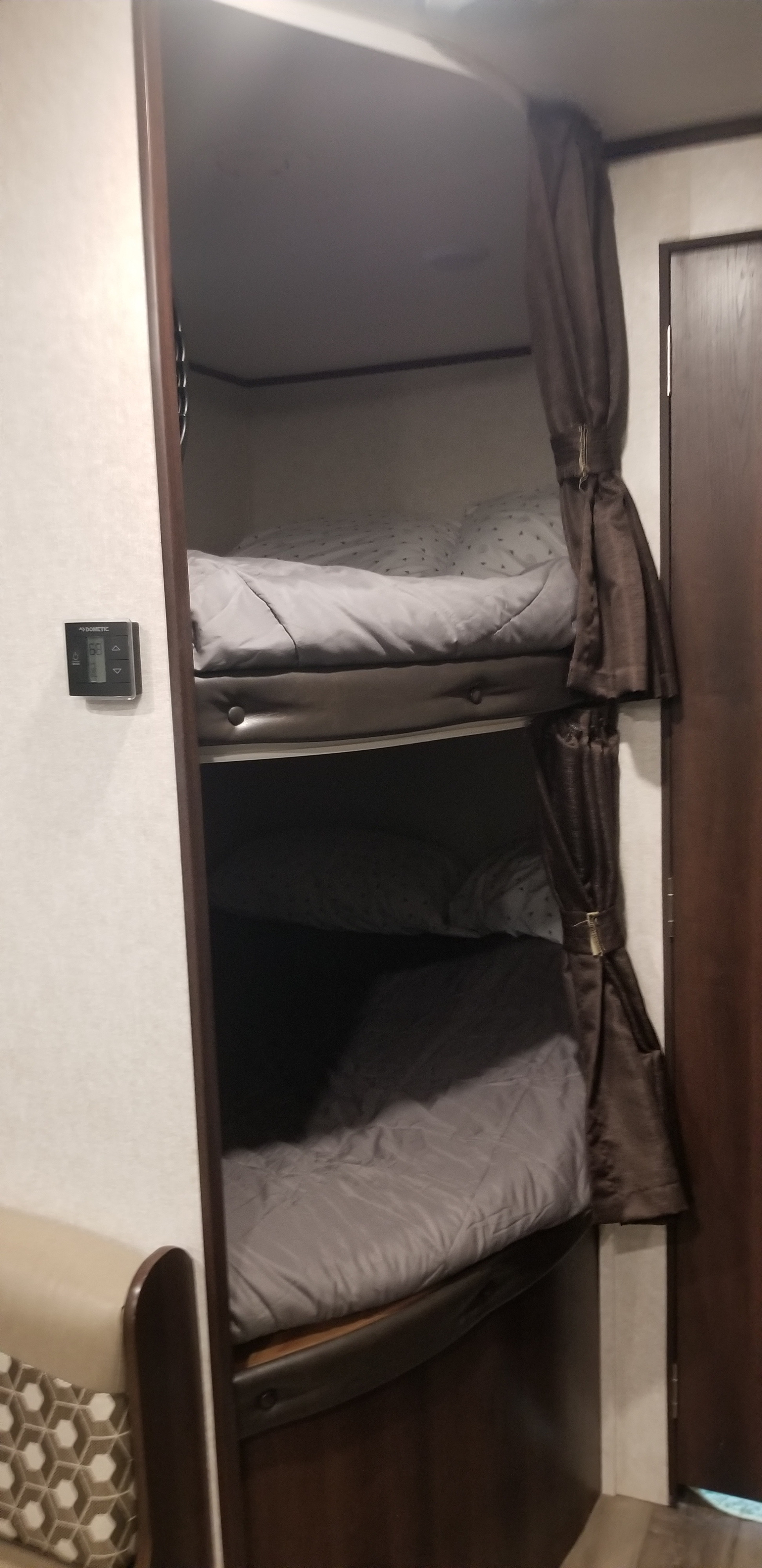 Inside an RV rental, cozy bunk beds with gray bedding and privacy curtains are shown. A Dometic thermostat reads 69 degrees.. Jayco Jay Flight SLX 2019