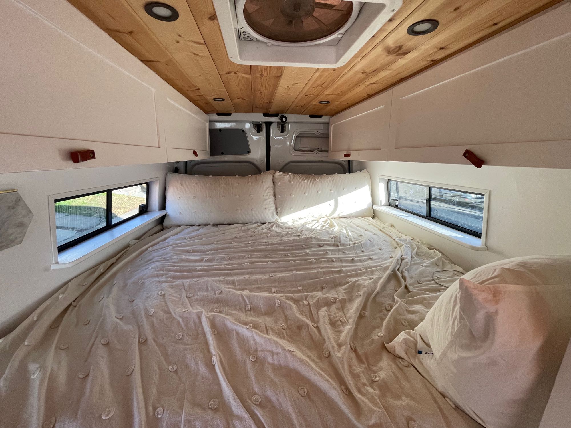 Cozy RV rental sleeping area: a large bed with textured white bedding, white overhead cabinets, and wood ceiling.. Mercedes Sprinter 2011