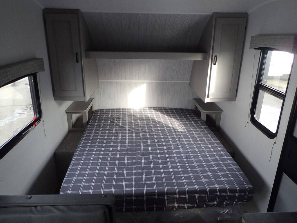 Cozy RV rental bedroom showing a plaid bed, overhead cabinets, and side windows, ready for your travels.. Coachmen Clipper 2024