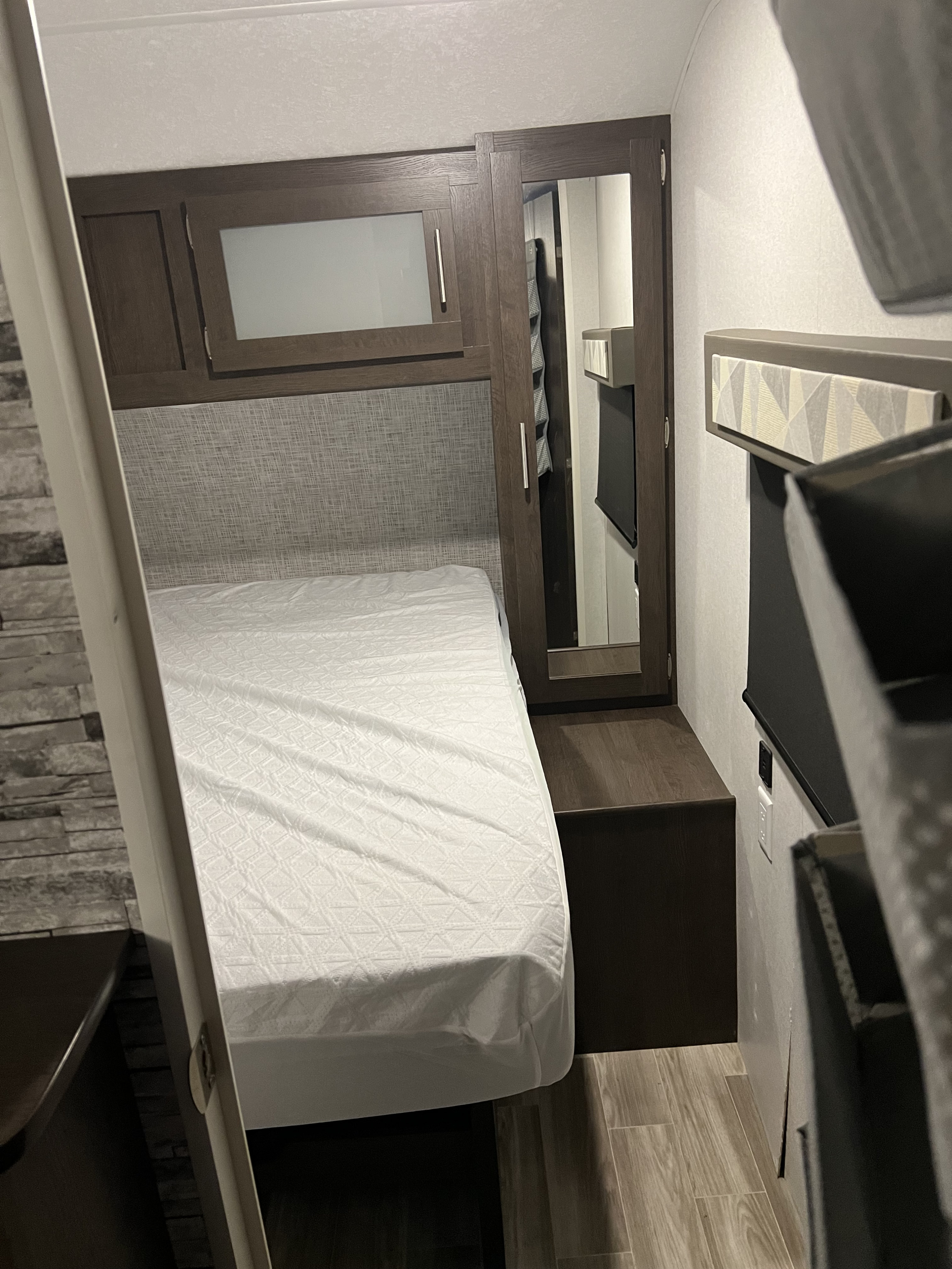 Inside an RV rental: a compact bedroom with a bed, overhead cabinets, mirrored closet, and wood-look floor.. Forest River Salem 2019