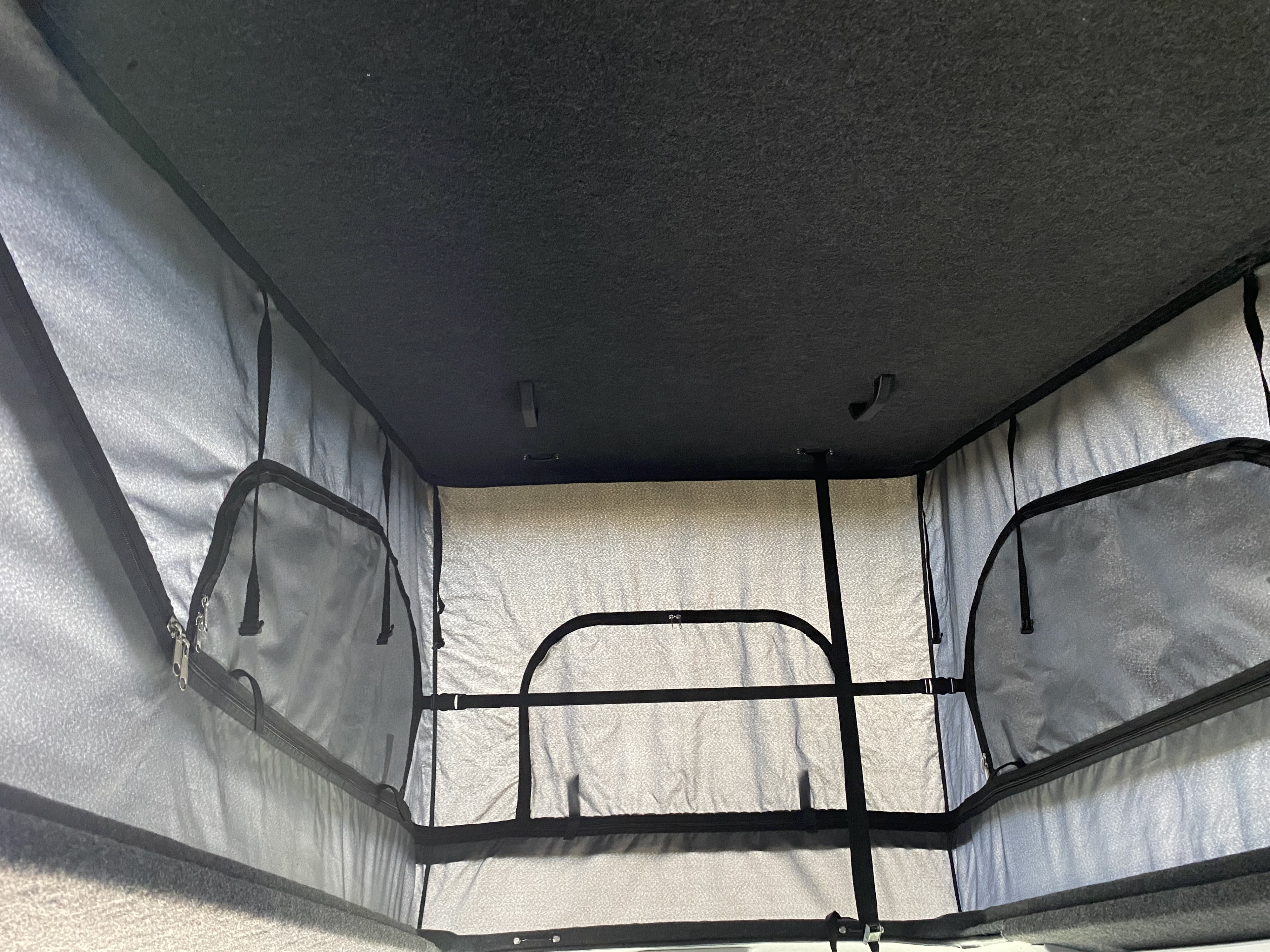 Interior view of an **RV rental** pop-top camper, showing the dark ceiling, light fabric walls, mesh windows/pockets, and bed frame.. Volkswagen VW T6 Camper 2017