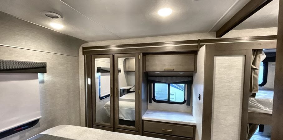 View inside an RV rental bedroom with mirrored closets, a built-in window seat, and bunk beds, offering comfort for trips.. Thor Motor Coach Four Winds 2025