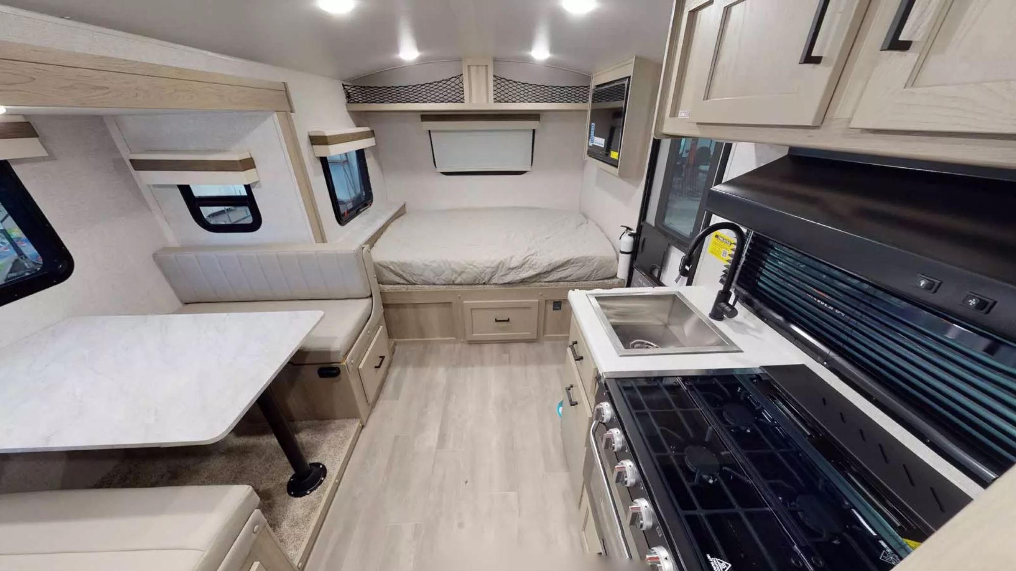 Full view of a bright rv rental interior, featuring a compact kitchen on the right, bed at the back, and dinette on the left.. Forest River Rockwood Geo Pro 2023