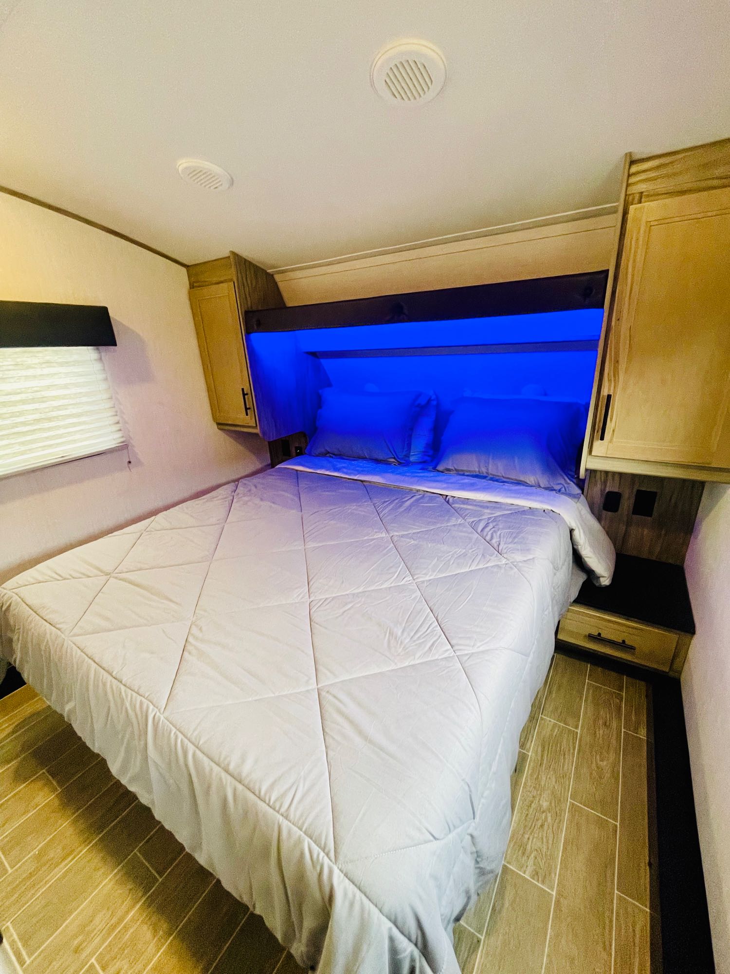 This cozy RV rental bedroom features a comfortable bed, vibrant blue accent lighting, built-in storage, and a window.. Forest River Cherokee Arctic Wolf 2022