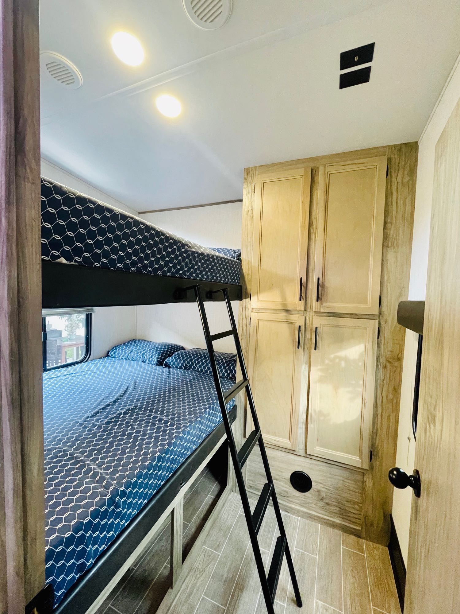 Cozy RV rental bunkhouse featuring comfy blue patterned beds, a ladder, and ample storage cabinets.. Forest River Cherokee Arctic Wolf 2022