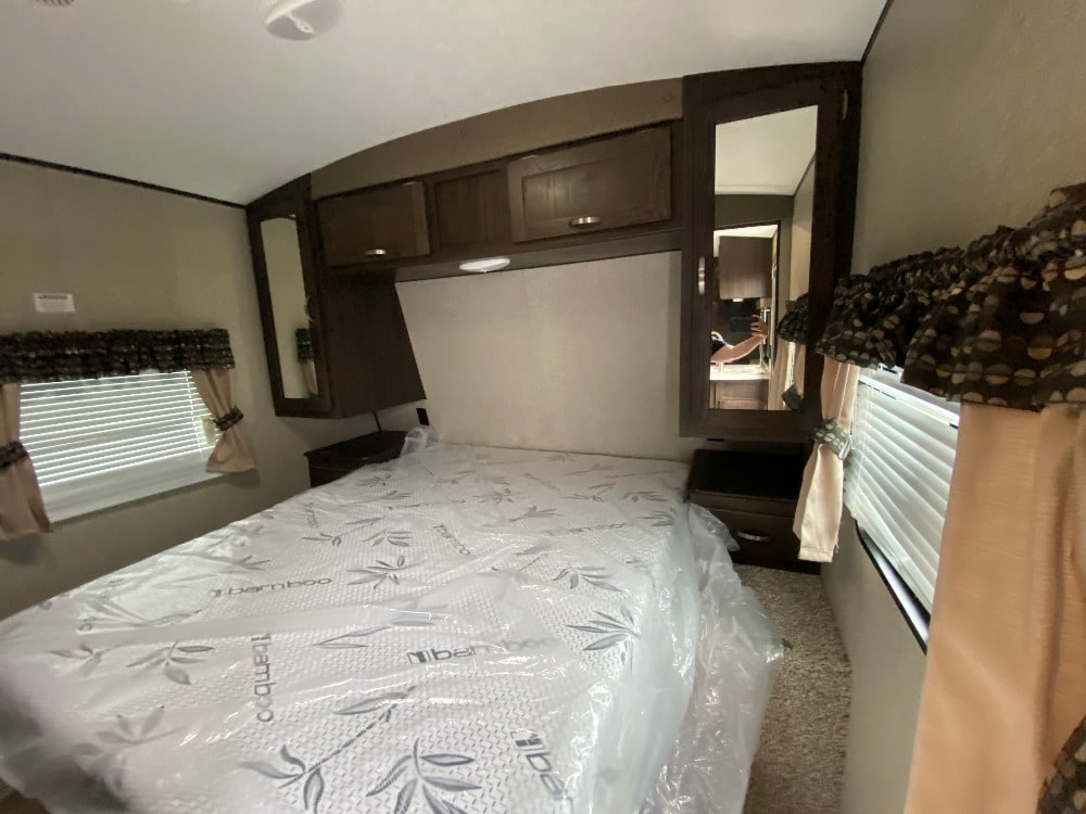 Cozy RV rental bedroom with a new mattress, overhead storage, mirrored wardrobes, and window views for travel adventures.. Keystone RV Springdale 2018