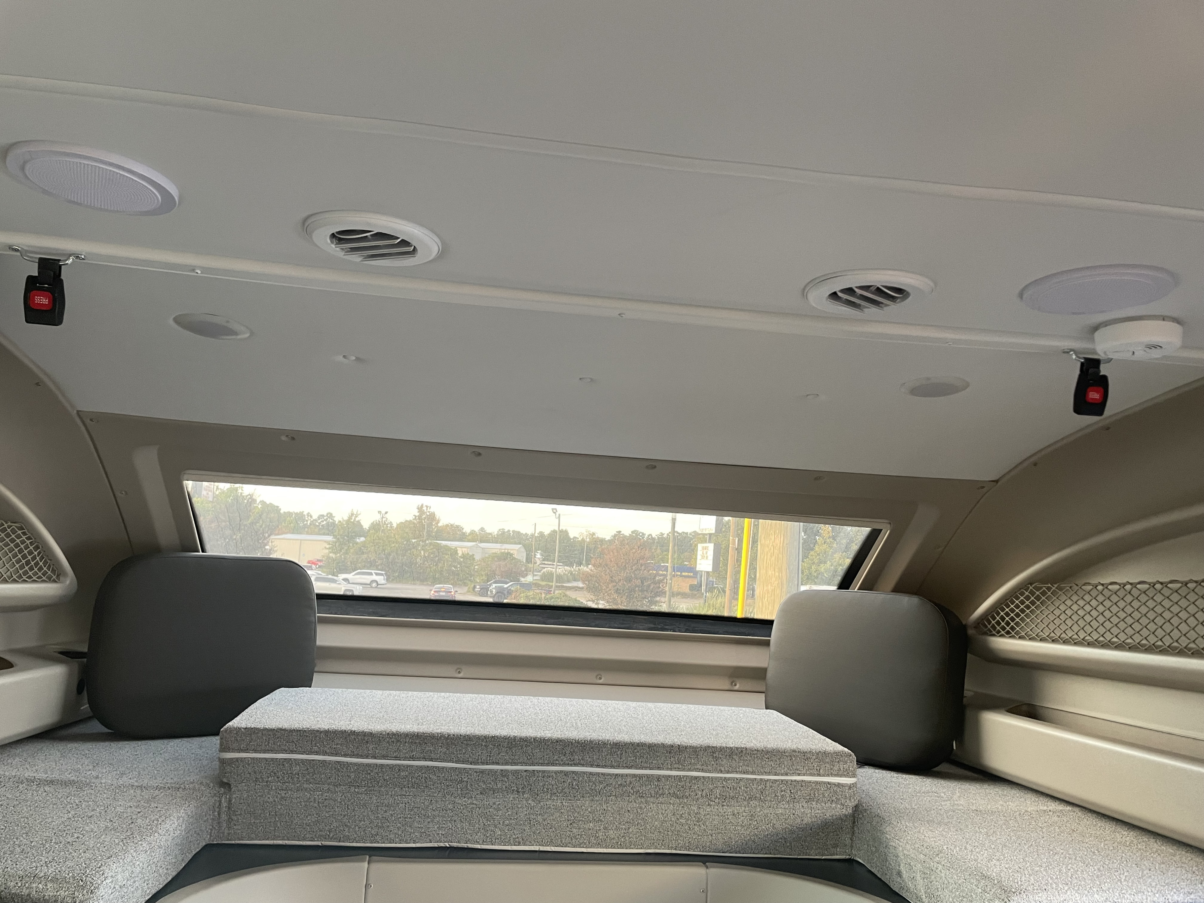 Inside an RV rental: a spacious overhead sleeping area with light grey cushions, ceiling vents, and window view.. Jayco Greyhawk 2023