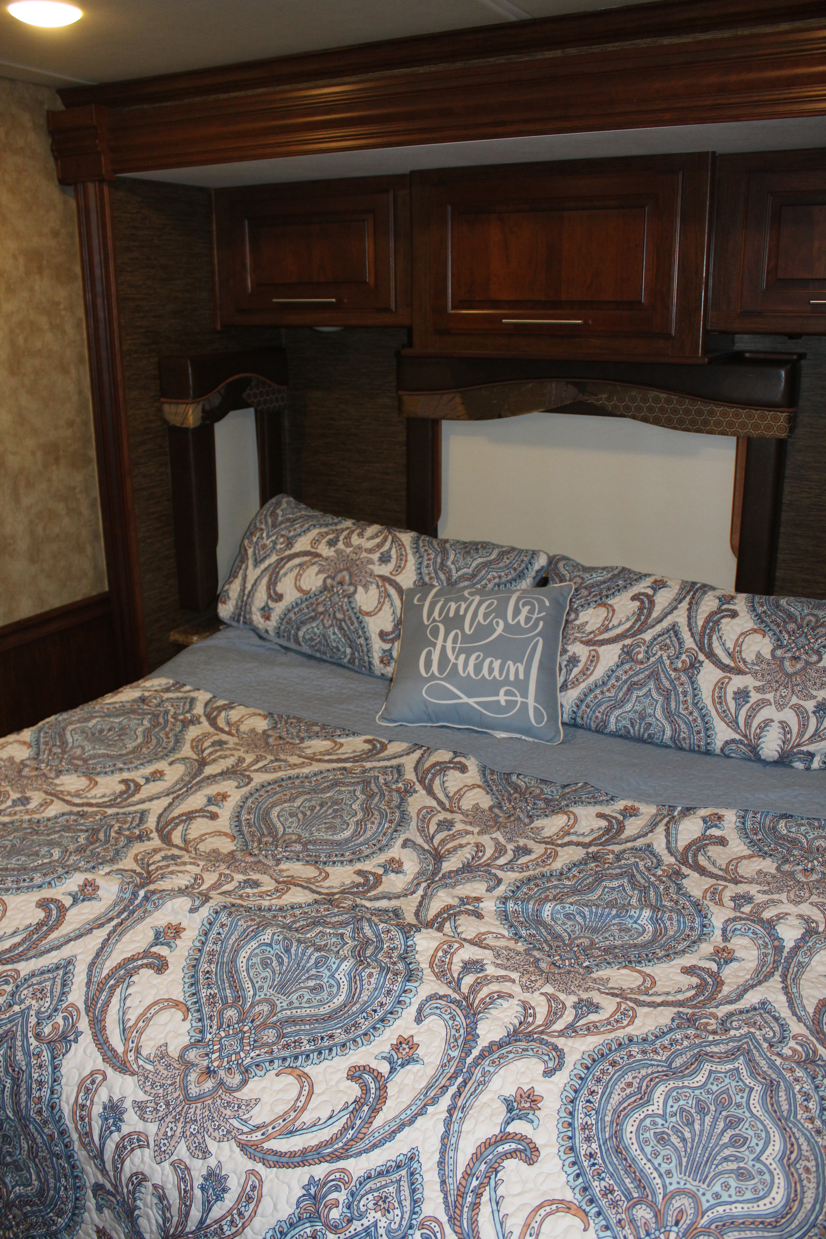 Cozy RV rental bedroom featuring a bed with blue and brown paisley bedding, "time to dream" pillow, & wood cabinets.. Coachmen 404rb 2017