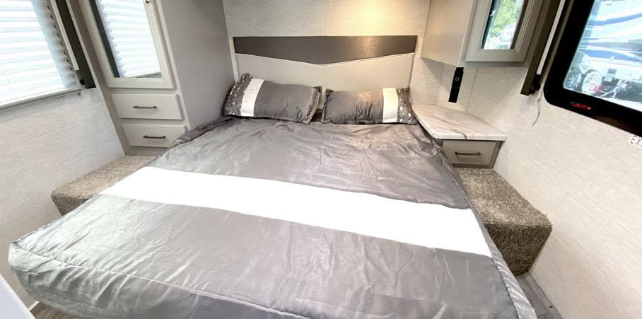 Cozy RV rental bedroom featuring a bed with gray bedding, built-in nightstands, and windows for natural light.. Thor Motor Coach Four Winds 2025