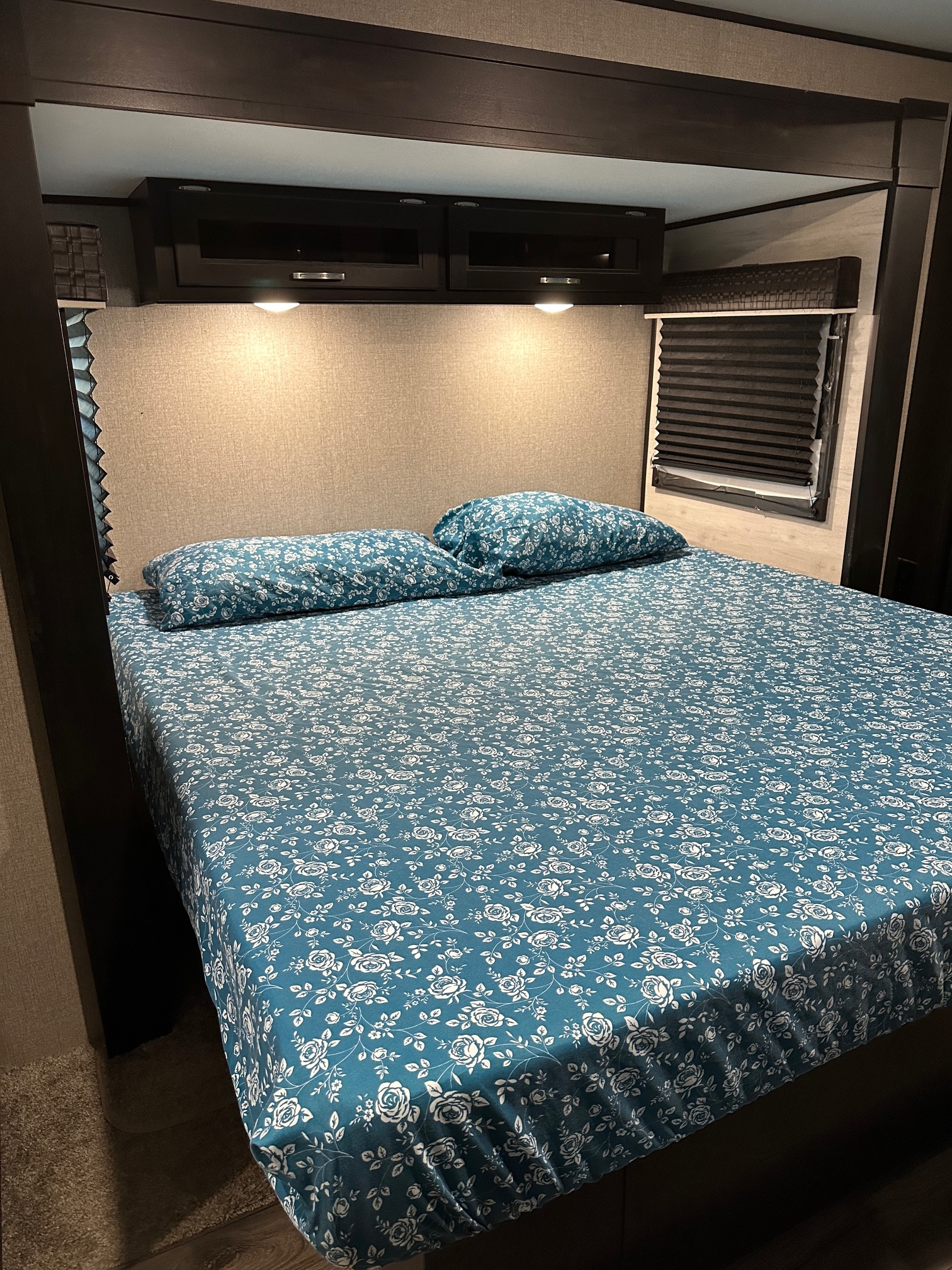 Cozy RV rental bedroom: bed with teal floral sheets, overhead storage, ambient lighting, and window blinds.. Jayco Jay Flight 2022