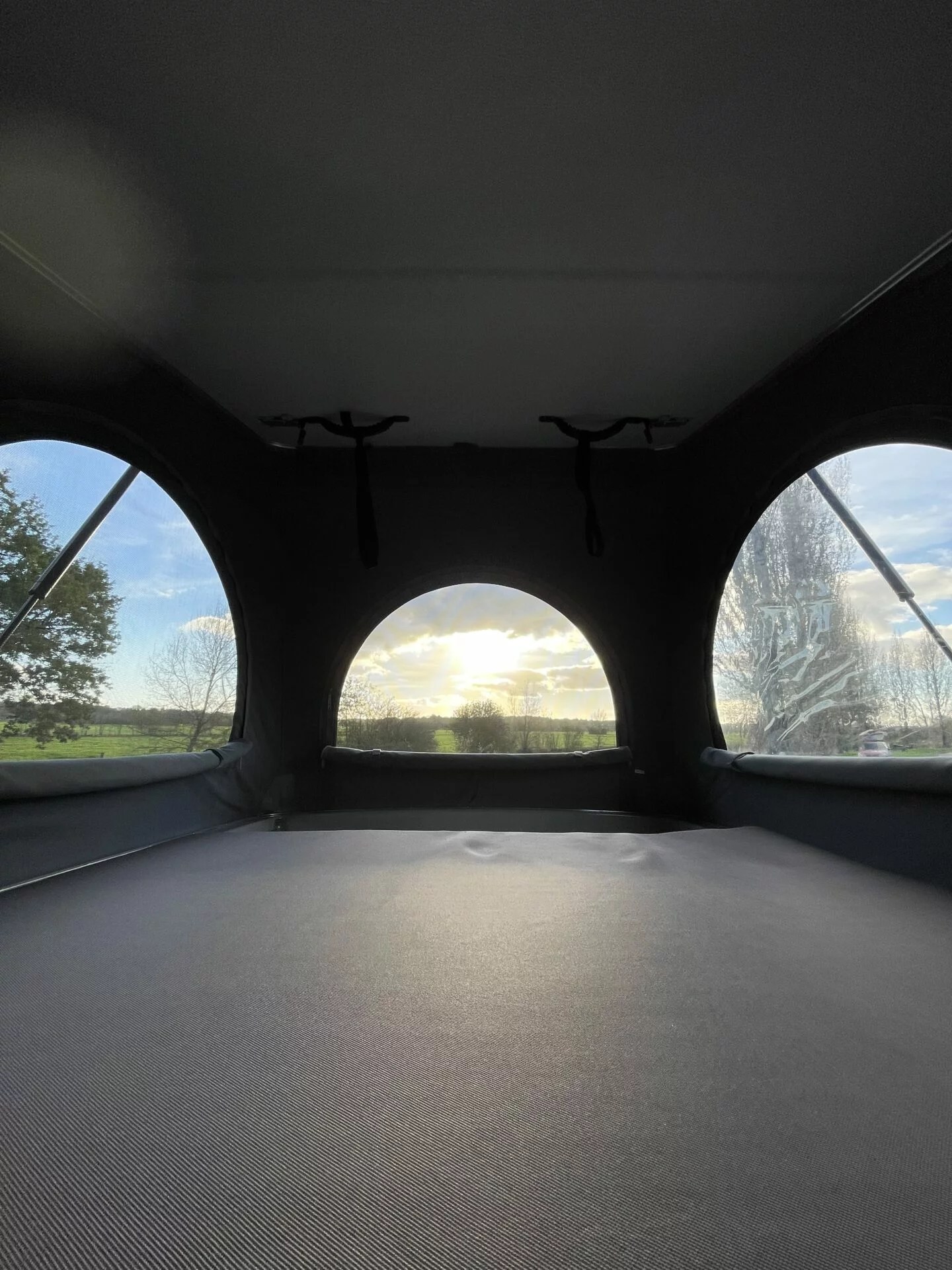 Relax in this RV rental pop-top camper's cozy bed with arched windows revealing a beautiful sunset over fields.. Volkswagen Summer 2024