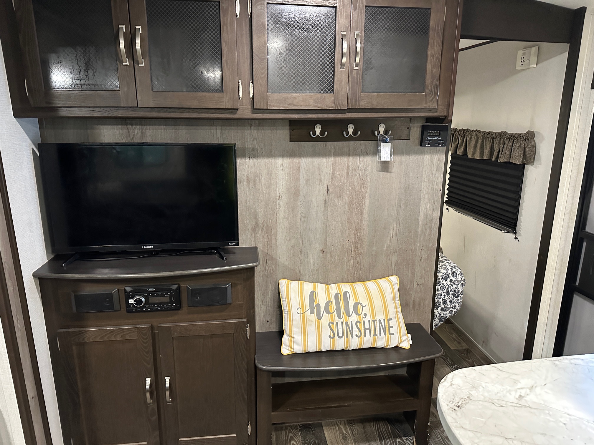 Cozy RV rental interior with TV, entertainment system, wooden cabinets, and a bench with a "hello sunshine" pillow, offering comfort.. Keystone RV Springdale 2020