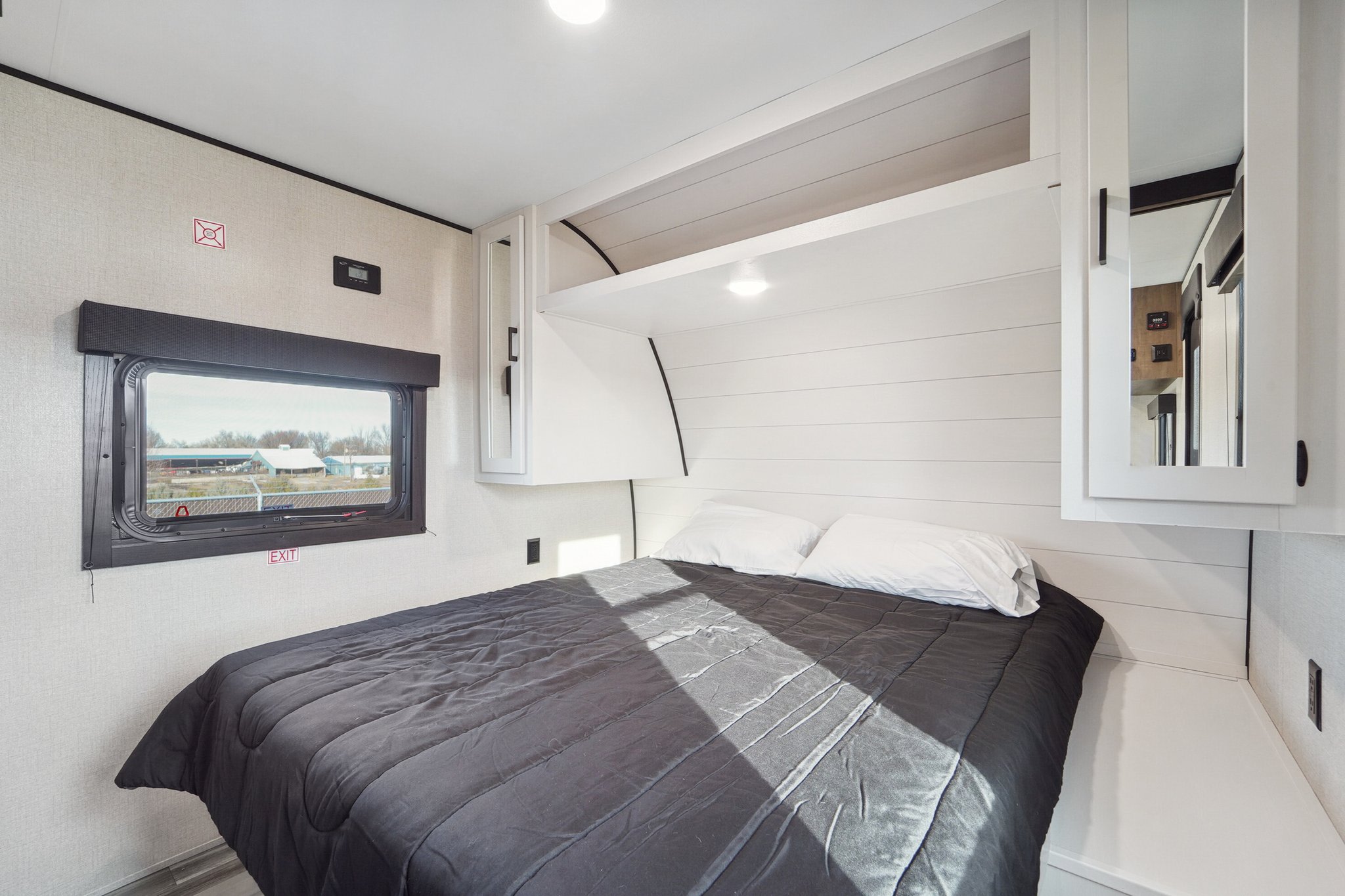 A cozy, modern RV rental bedroom with a dark comforter, white cabinets, and a window. Perfect for comfortable travel.. Wayfinder Goplay 2024