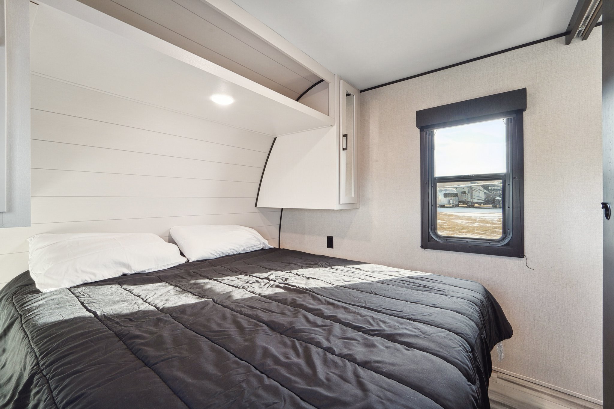 Inside a modern RV rental: a cozy bedroom with shiplap walls, comfortable bed, overhead storage, and outdoor view.. Wayfinder Goplay 2024