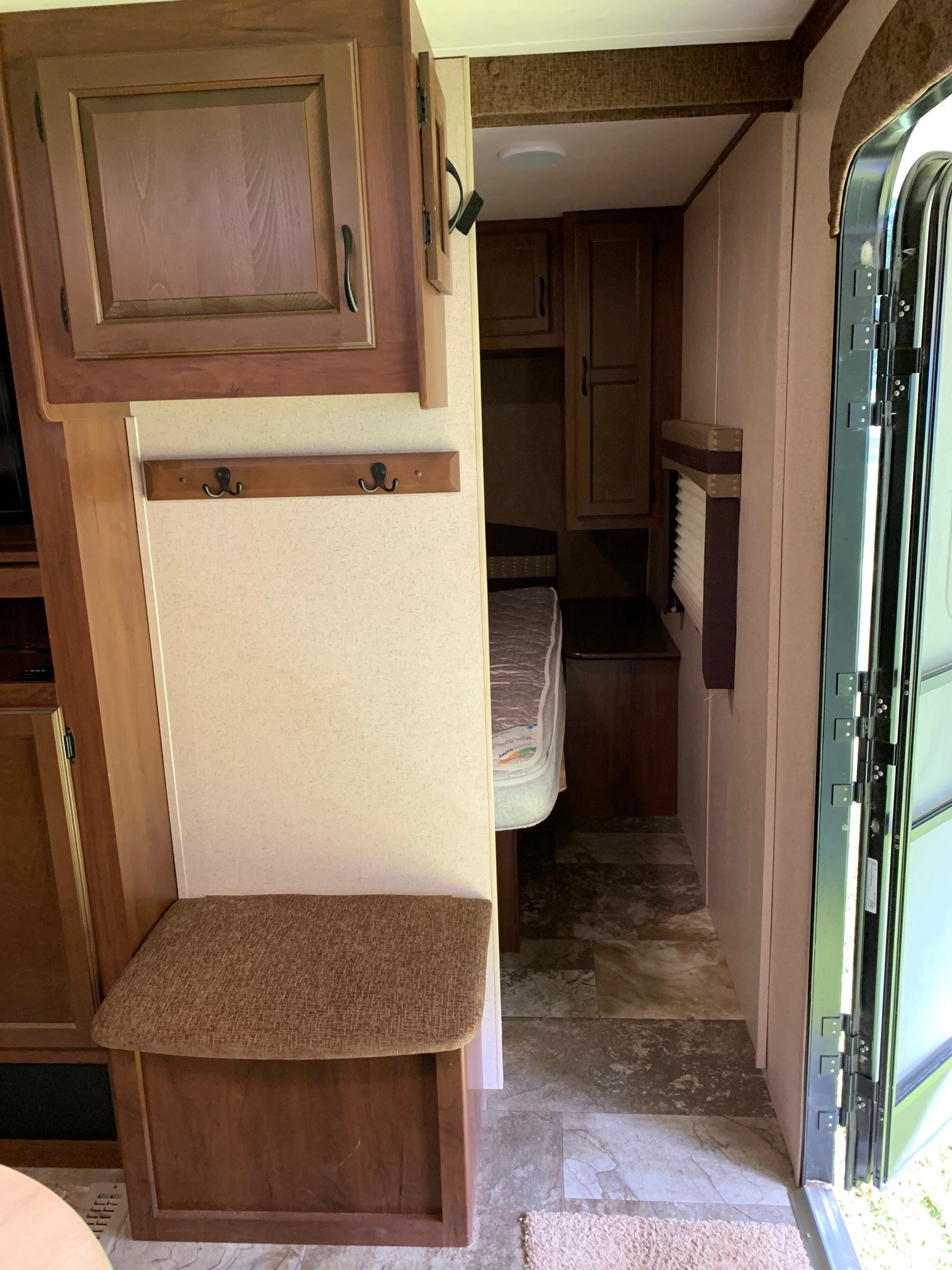 Explore a comfortable RV rental interior. It features wood cabinets, a coat rack, cushioned bench, and a cozy sleeping area.. Jayco Jay Flight 2015