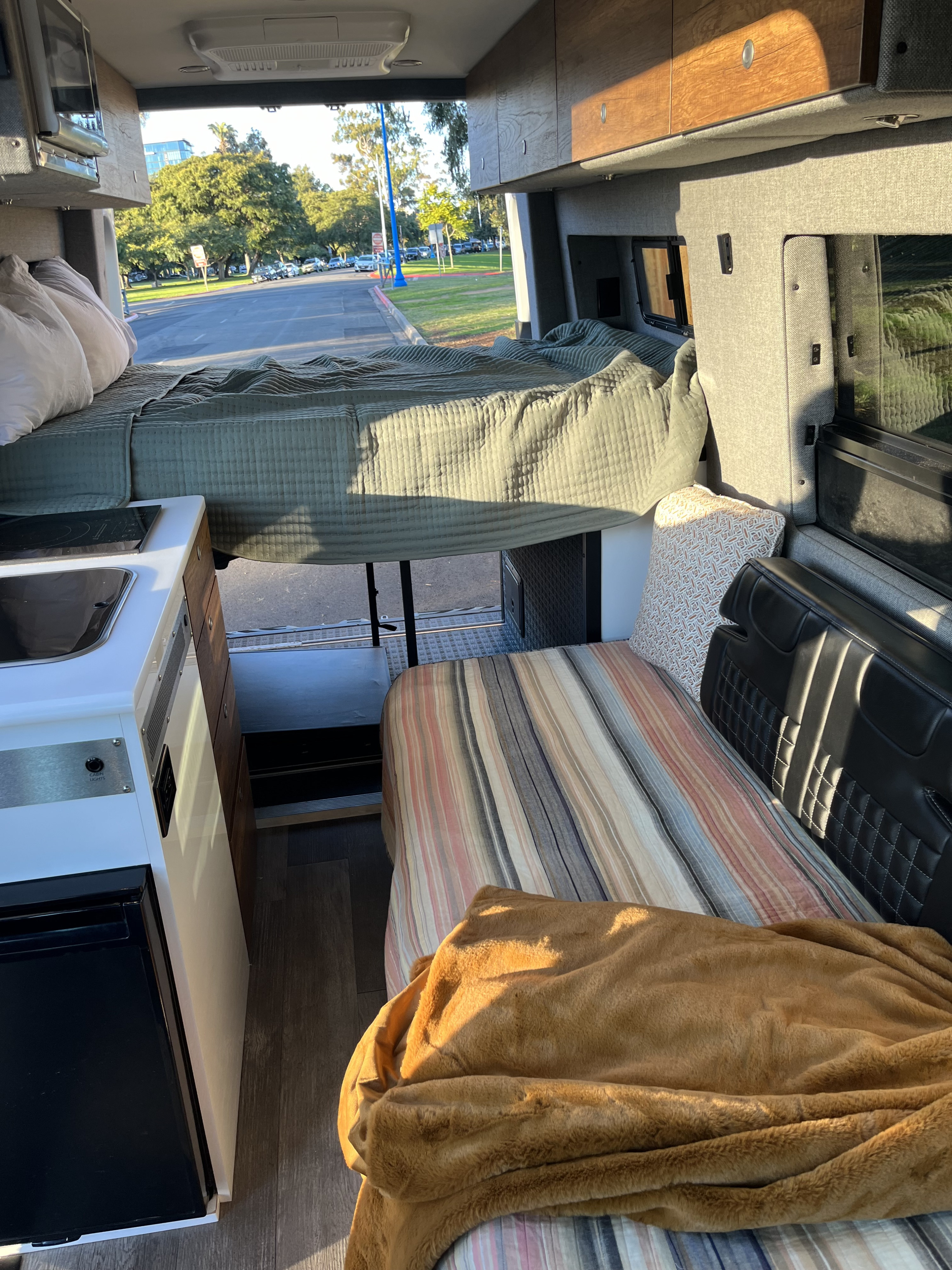 Sunlit RV rental interior featuring a raised bed, compact kitchen, and lower sleeping/seating area.. Storyteller Overland Storyteller Overland Class B 2020