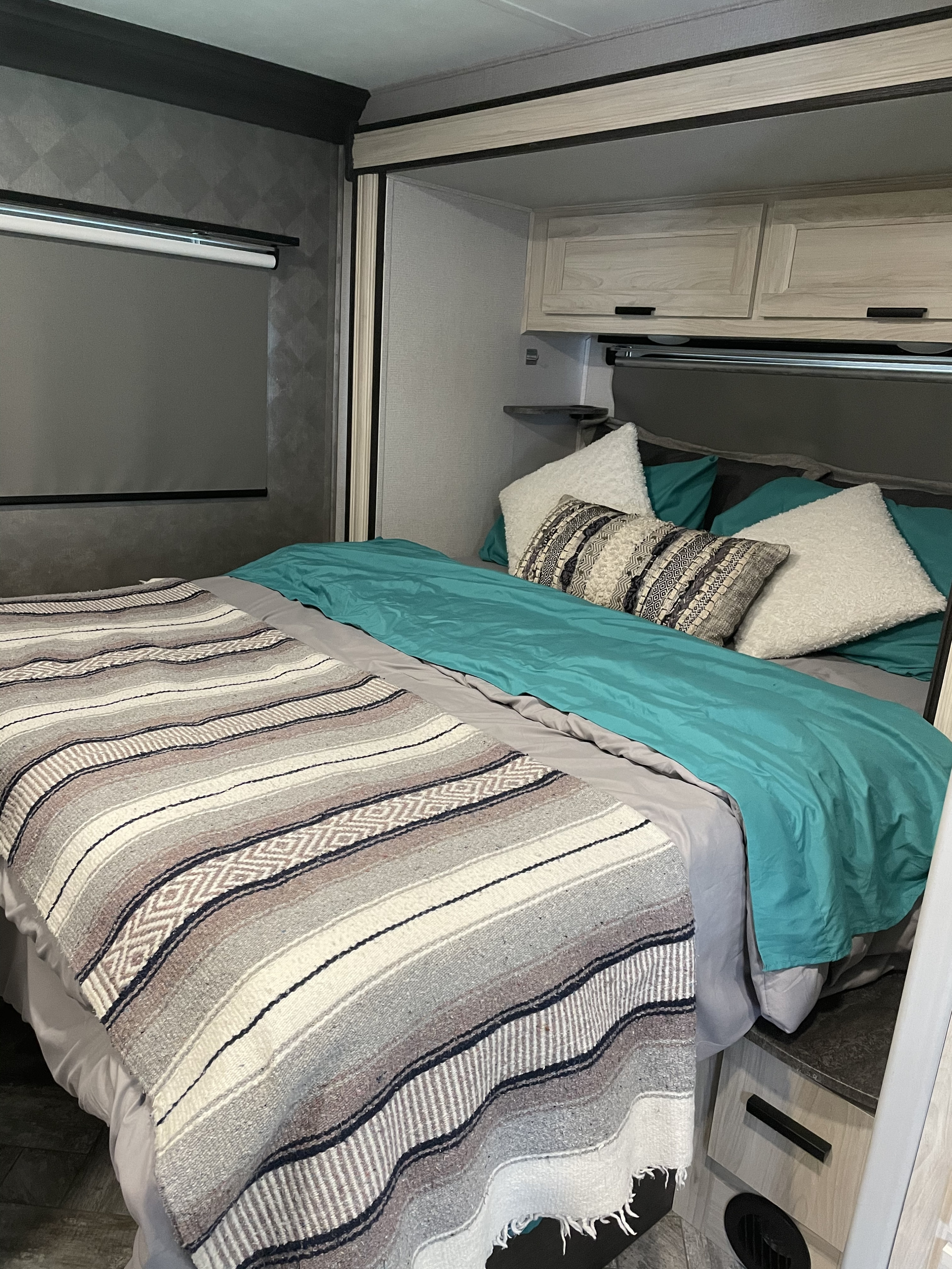 Cozy RV rental bedroom with teal bedding, patterned blanket, and overhead cabinets for a comfortable stay.. Forest River Sunseeker LE 2021