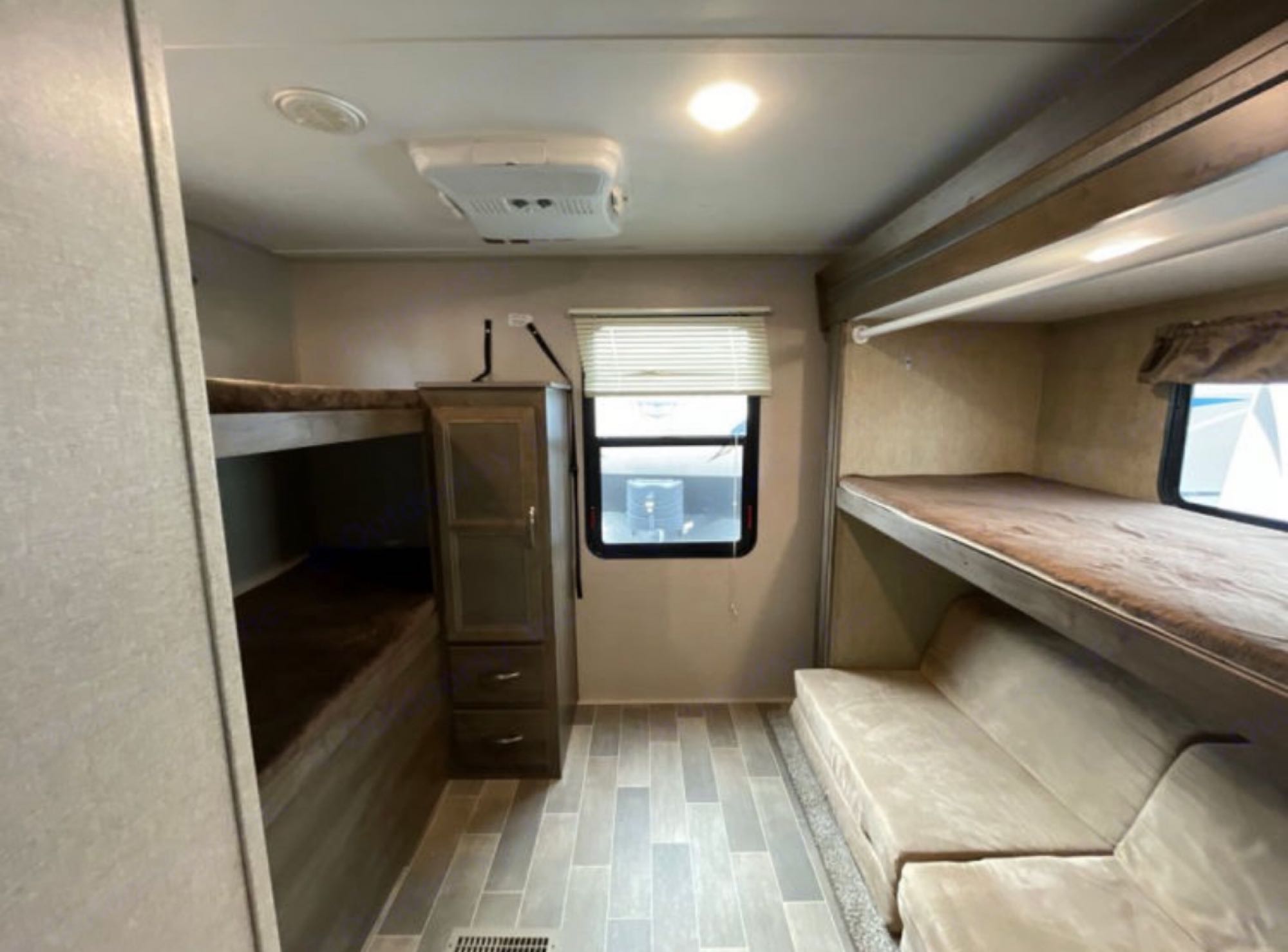 RV rental interior: Bunk beds on both sides, with a sofa below the right bunk. Features window, AC, wood-look floor. Camper.. Dutchmen Coleman Light 2018