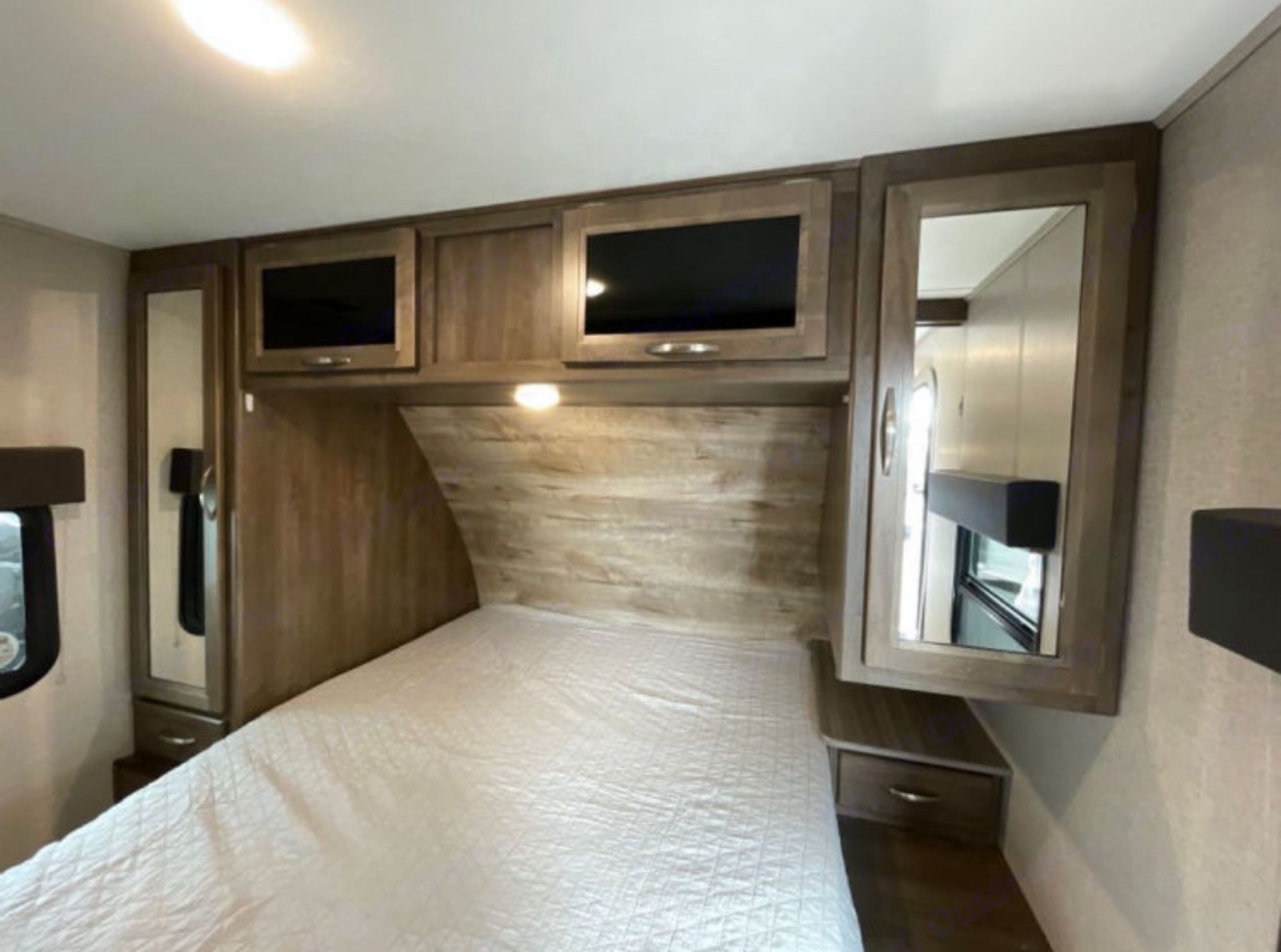RV rental bedroom shows a bed, wood cabinets with mirrors, and overhead storage for a cozy travel space.. Dutchmen Coleman Light 2018