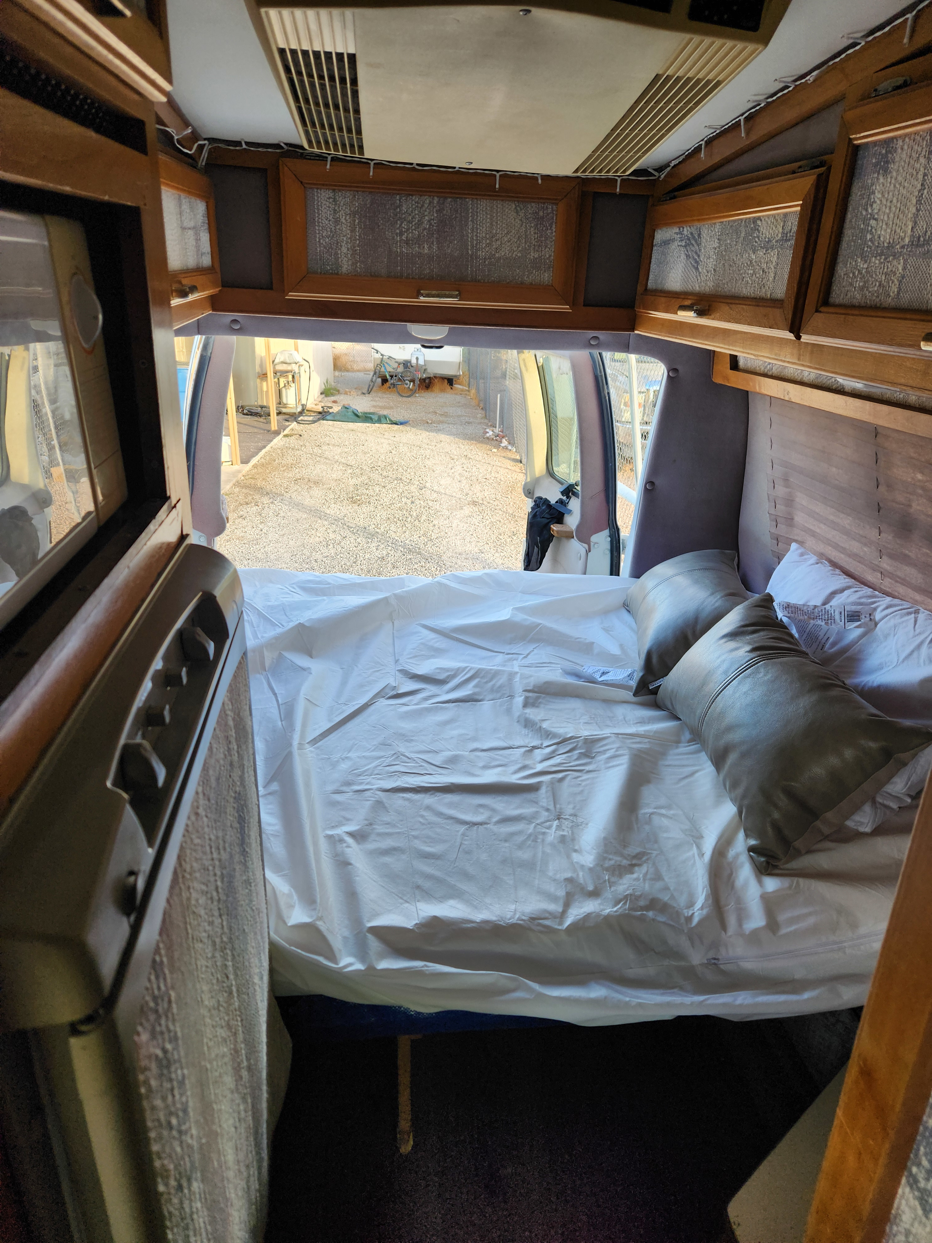 Cozy camper van interior, perfect for an rv rental, featuring a comfortable bed, overhead cabinets, and open rear doors to the outside.. Dodge B Van 1994